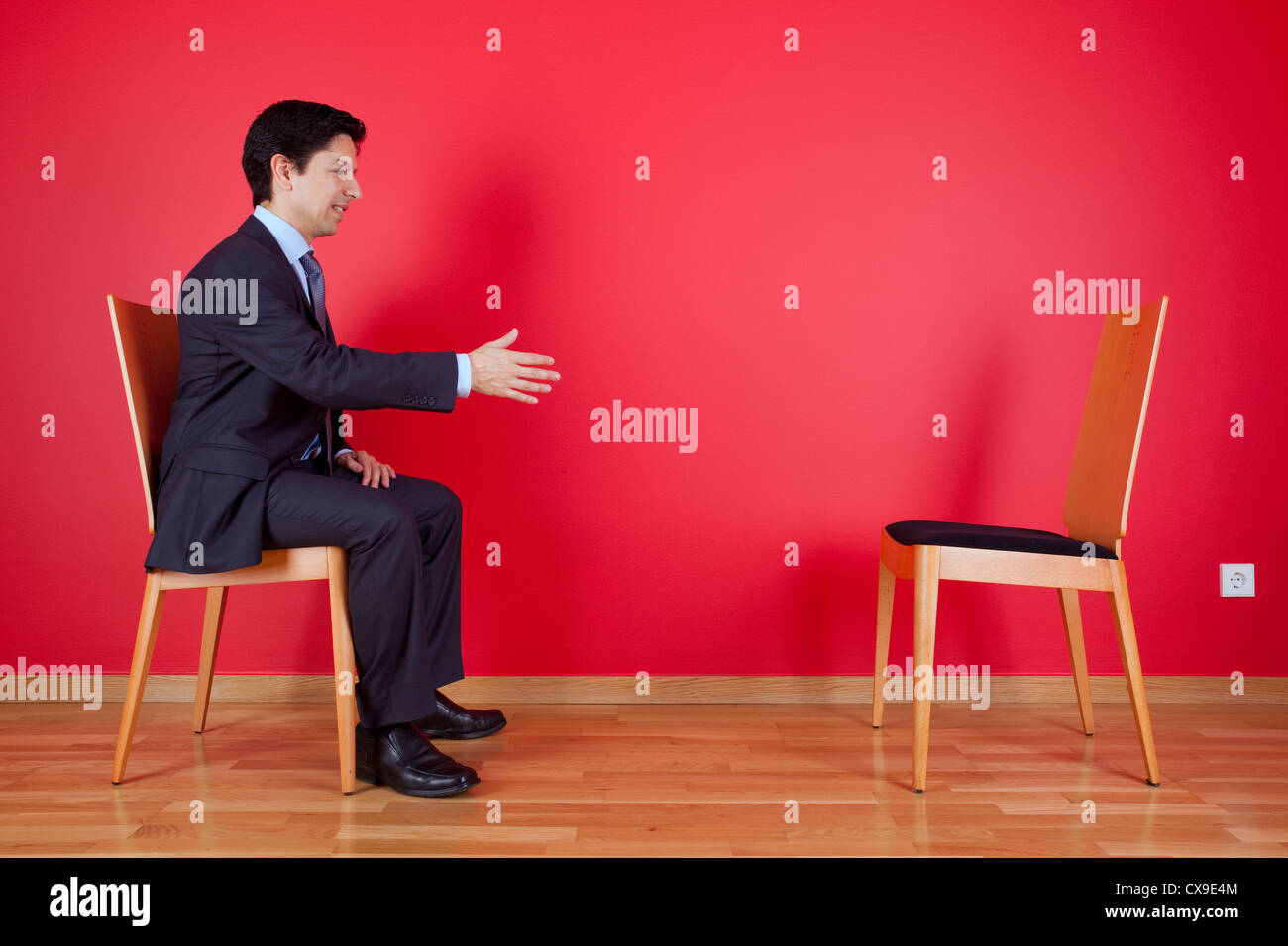 Accordo di stretta di mano tra un imprenditore e una sedia accanto ad una parete rossa Foto Stock