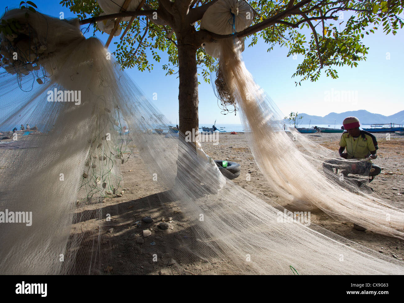 L'uomo riassettando le reti da pesca su una spiaggia, Dili, Timor orientale Foto Stock