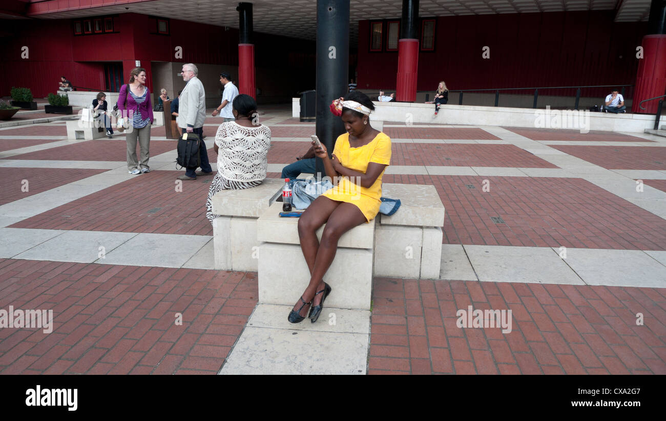 Nero donna africana in abito giallo texting sul telefono cellulare al di fuori nella British Library piazza Londra Inghilterra REGNO UNITO Foto Stock