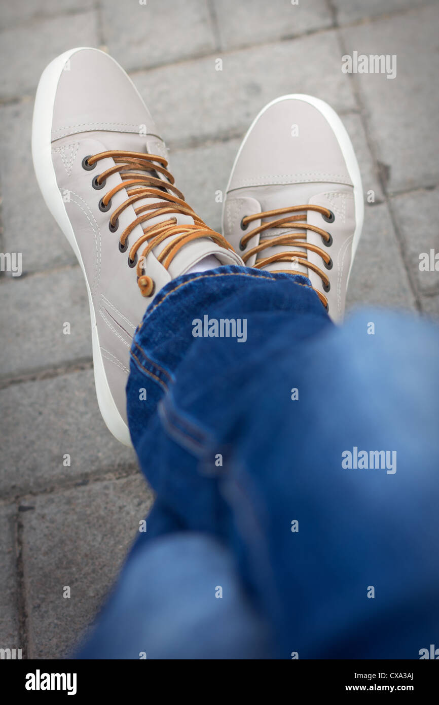 Metà di corpo di un adolescente di sesso maschile, ponendo egli jeans e scarpe da ginnastica, seduta piede a croce Foto Stock