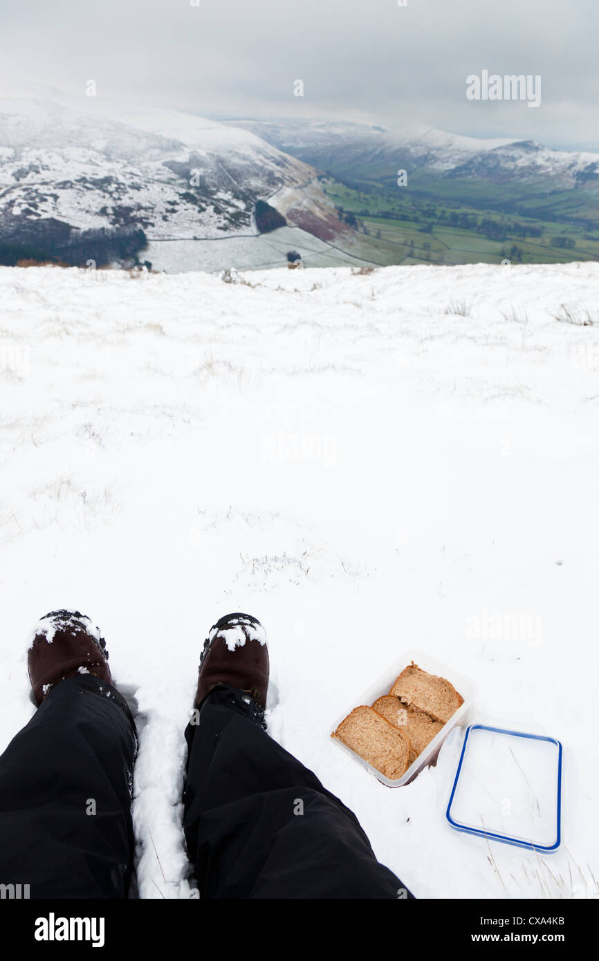 Escursionista con panini confezionati in una scatola di pranzo sulla cima di una collina nella neve invernale, Derbyshire, Peak District, England, Regno Unito Foto Stock