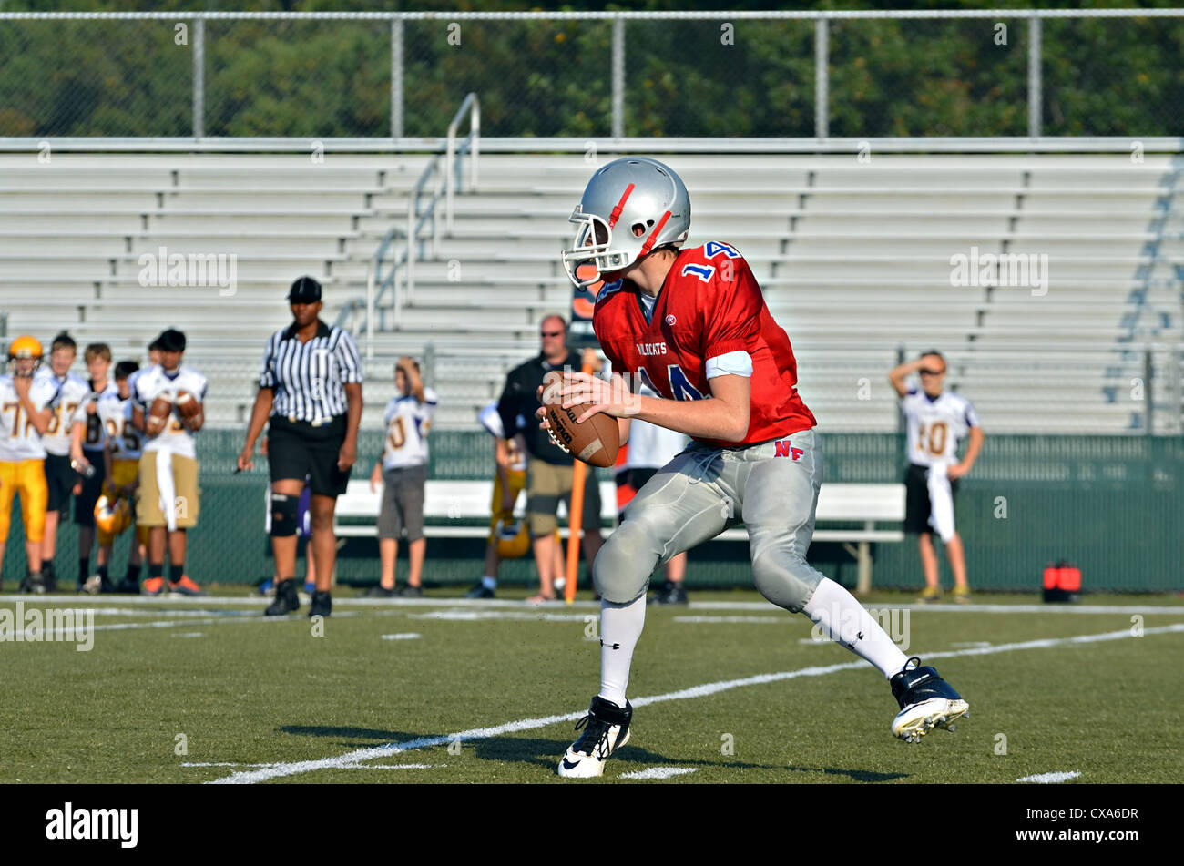 Un giovane quarterback pronto a lanciare la palla durante una partita di calcio, un arbitro seguendo da vicino l'azione. Foto Stock