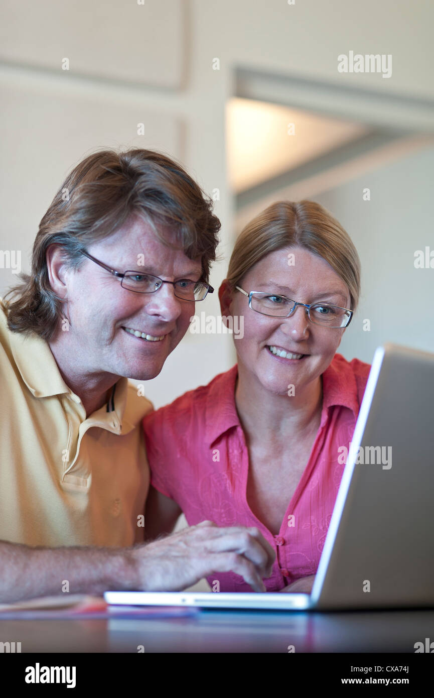 Coppia attraente a casa utilizzando il loro computer portatile insieme, alla luce del vivere contemporaneo ufficio in camera. Foto Stock