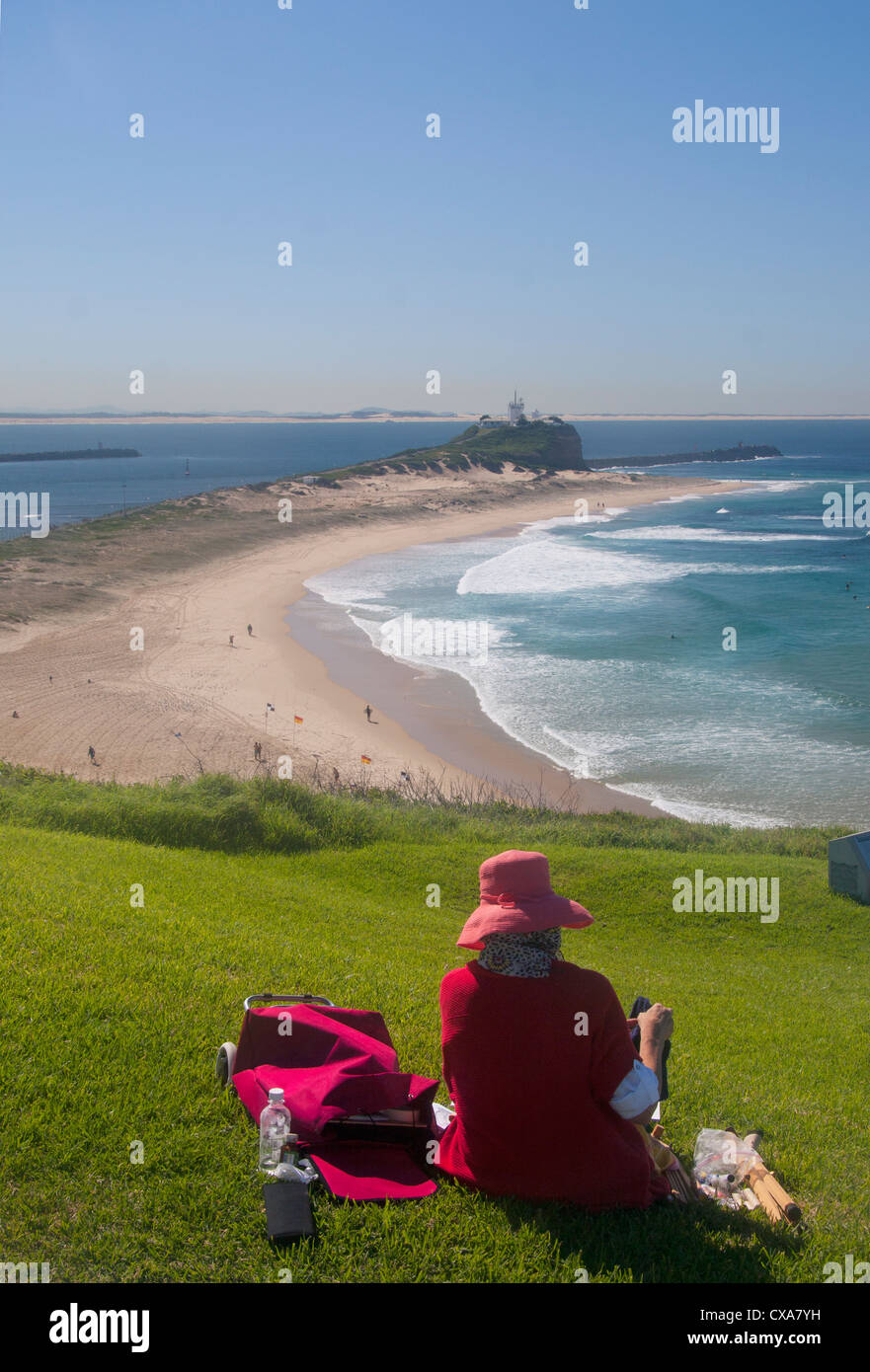 Donna che indossa cappello rosso seduto su erba a Fort Scratchley Nobbys affacciato sulla spiaggia e sul faro Newcastle NSW Australia Foto Stock