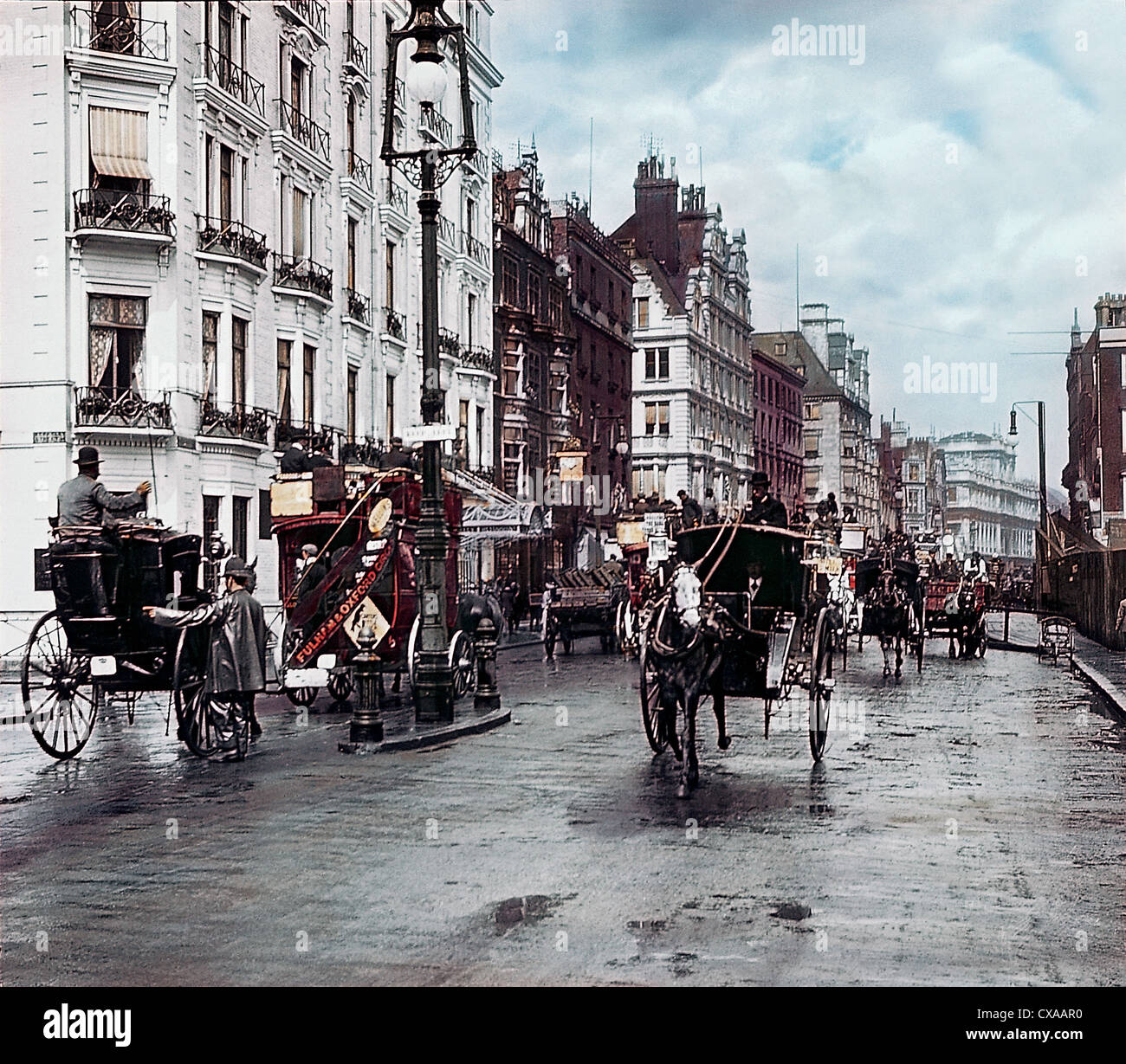 Vista colorata delle carrozze trainate da cavalli che viaggiano in entrambe le direzioni su Oxford Street, Londra, Inghilterra, 1897. Un poliziotto si trova nella strada che dirige il traffico. (Foto di Burton Holmes) Foto Stock