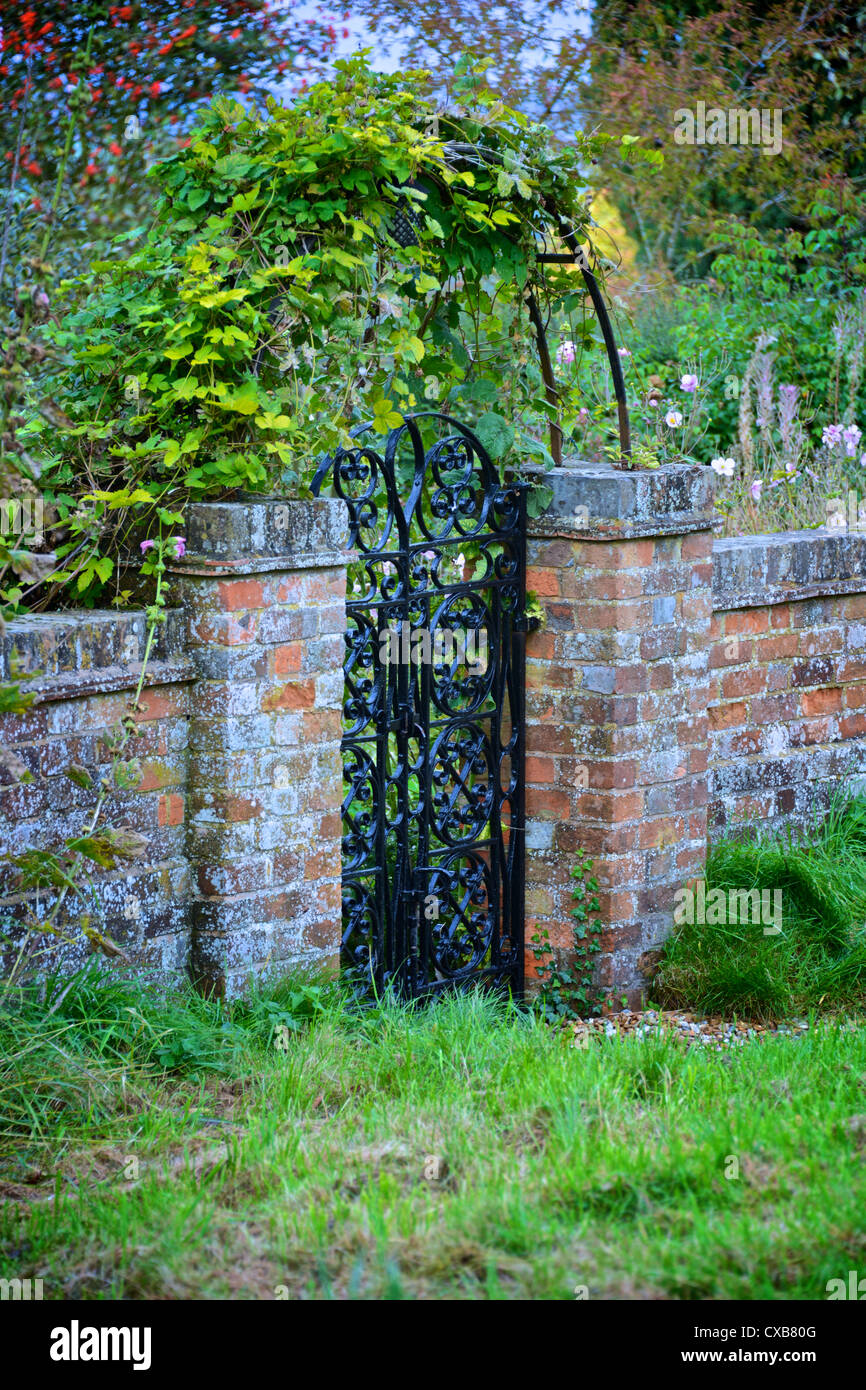 Garden Gate e arch con vecchi mattoni rossi e parete verde della vigna, bacche rosse e giardino prato Foto Stock