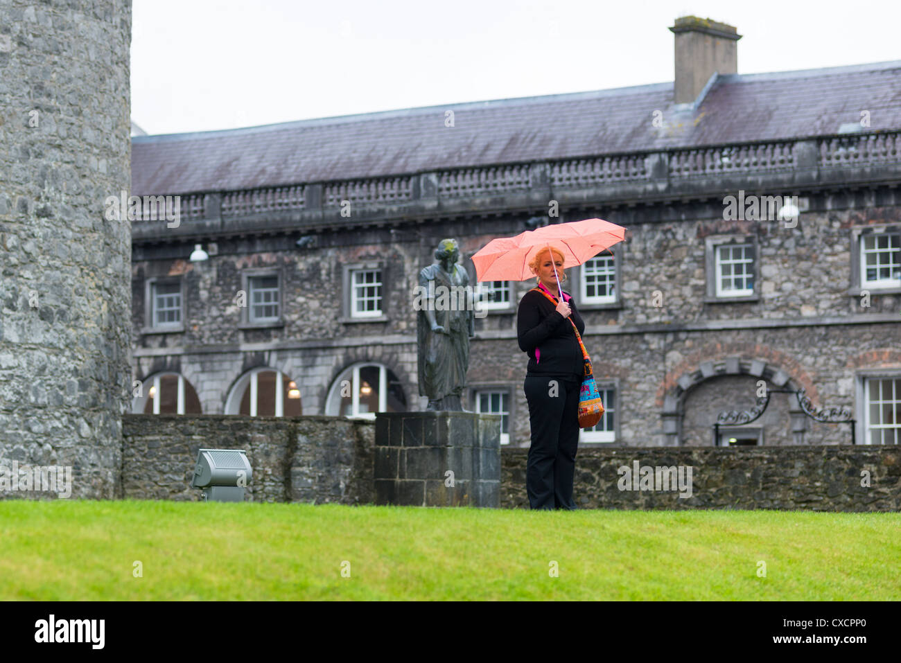 La donna sta sotto la pioggia a Kilkenney Castello con il design center per la parte posteriore, Repubblica di Irlanda. Foto Stock