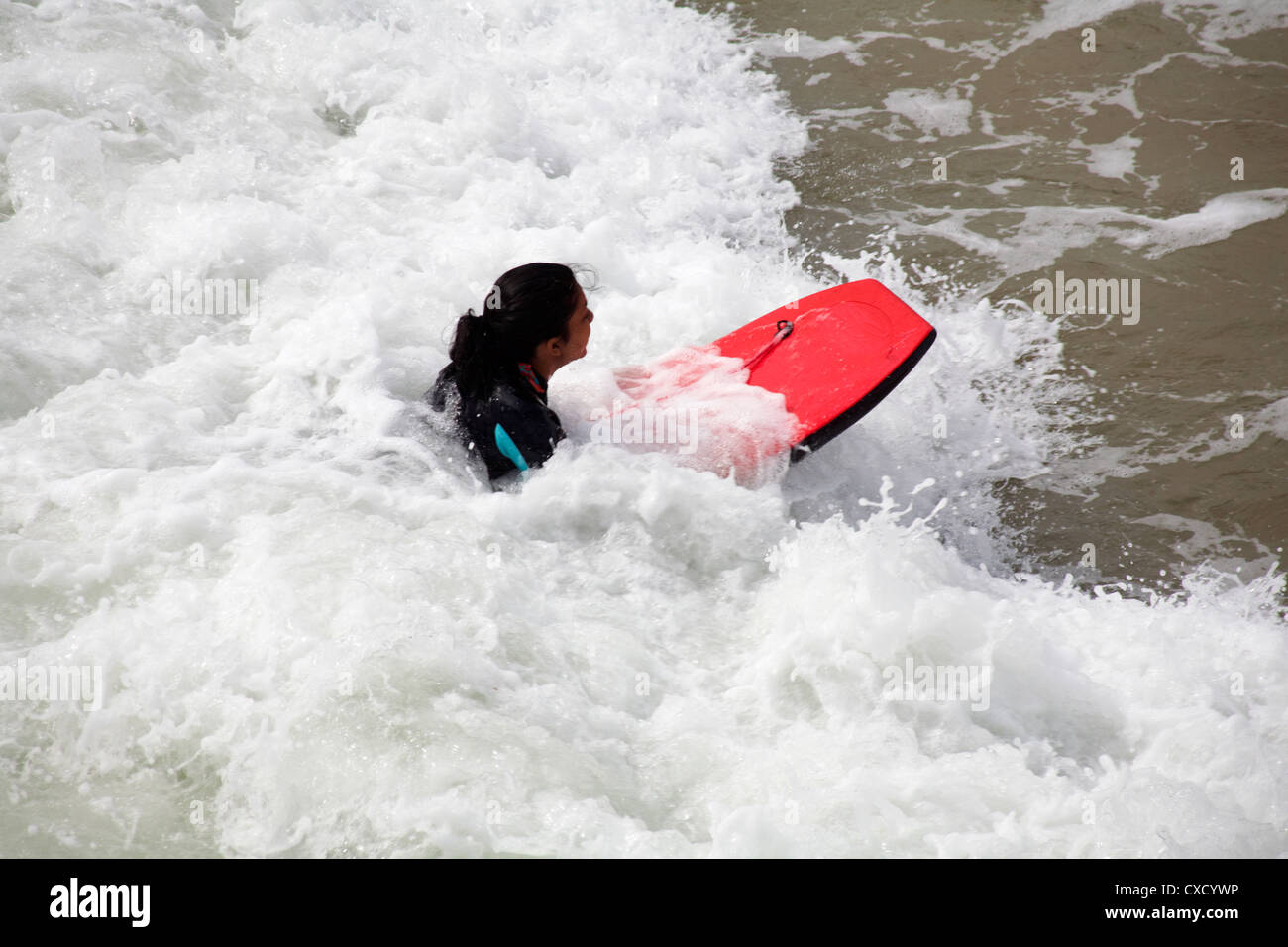 Femmina con corpo board Surf le onde a Boscombe Beach, Bournemouth in agosto Foto Stock