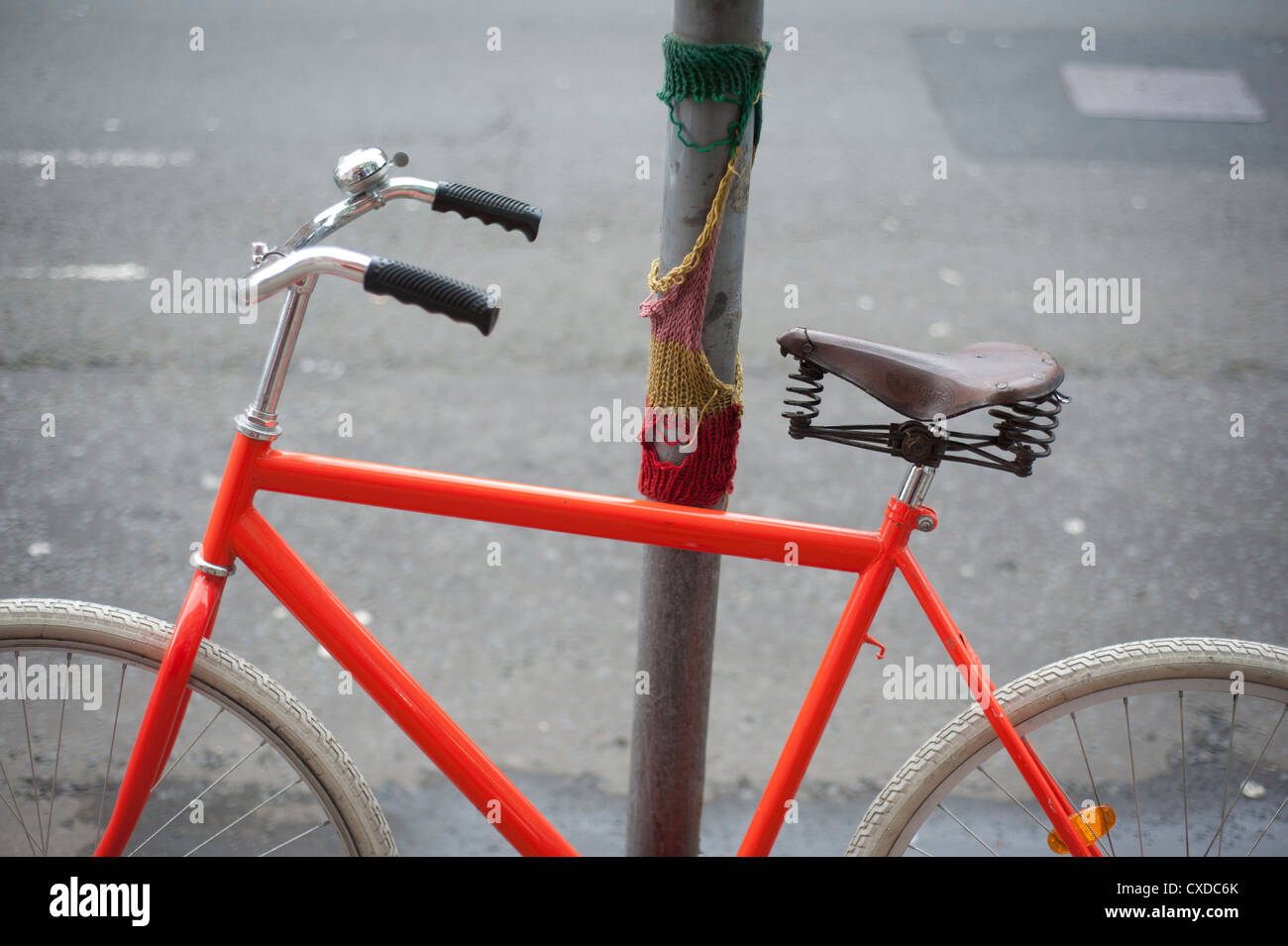 Orange singola velocità ingranaggio fisso bici da corsa con pneumatici bianco incatenato in una città lampione con maglia graffiti. Foto Stock