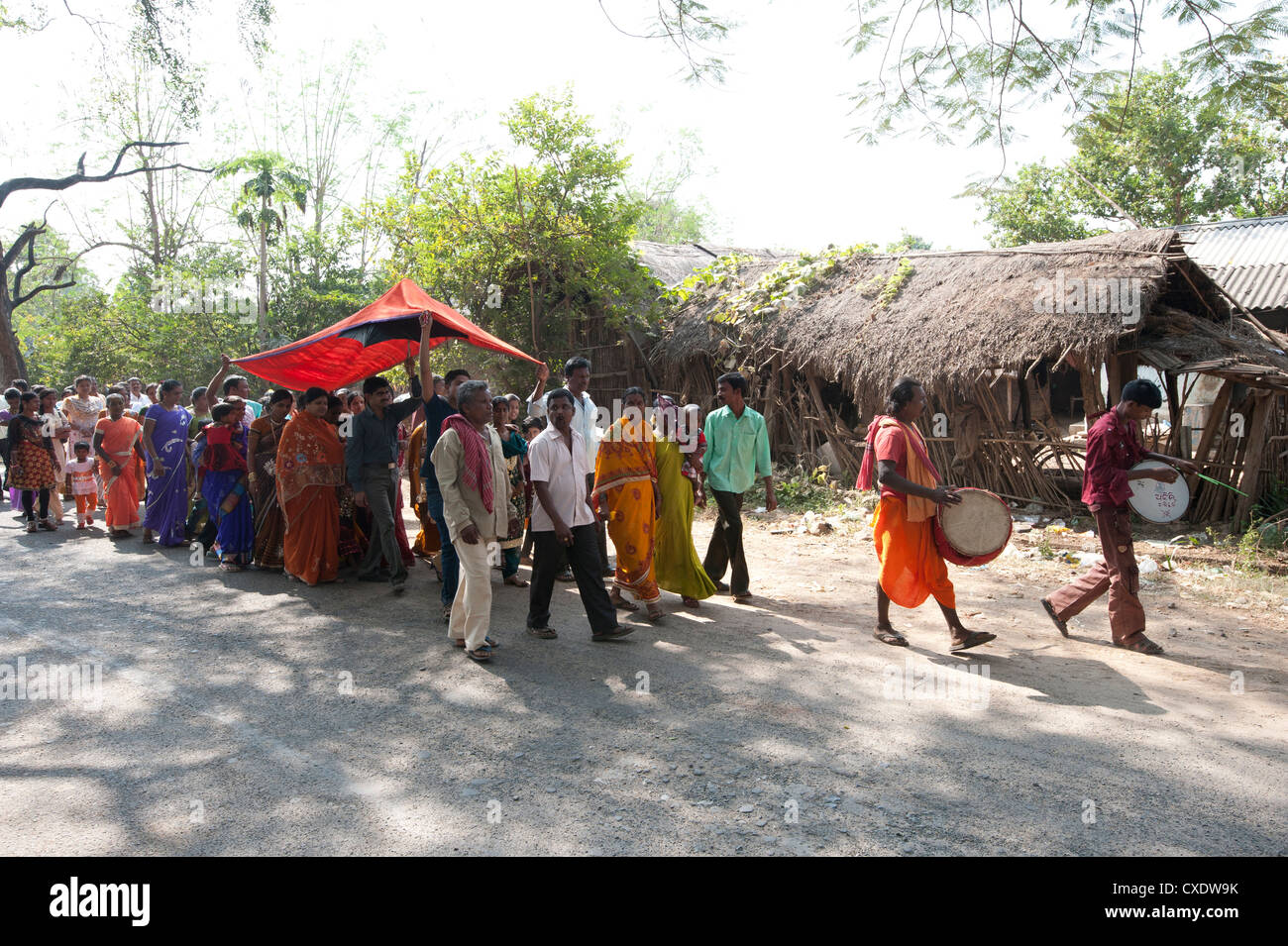 I percussionisti villaggio leader sposa sotto la tettoia rossa per la sua cerimonia di matrimonio in una processione con la famiglia e gli abitanti di un villaggio rurale, Orissa Foto Stock