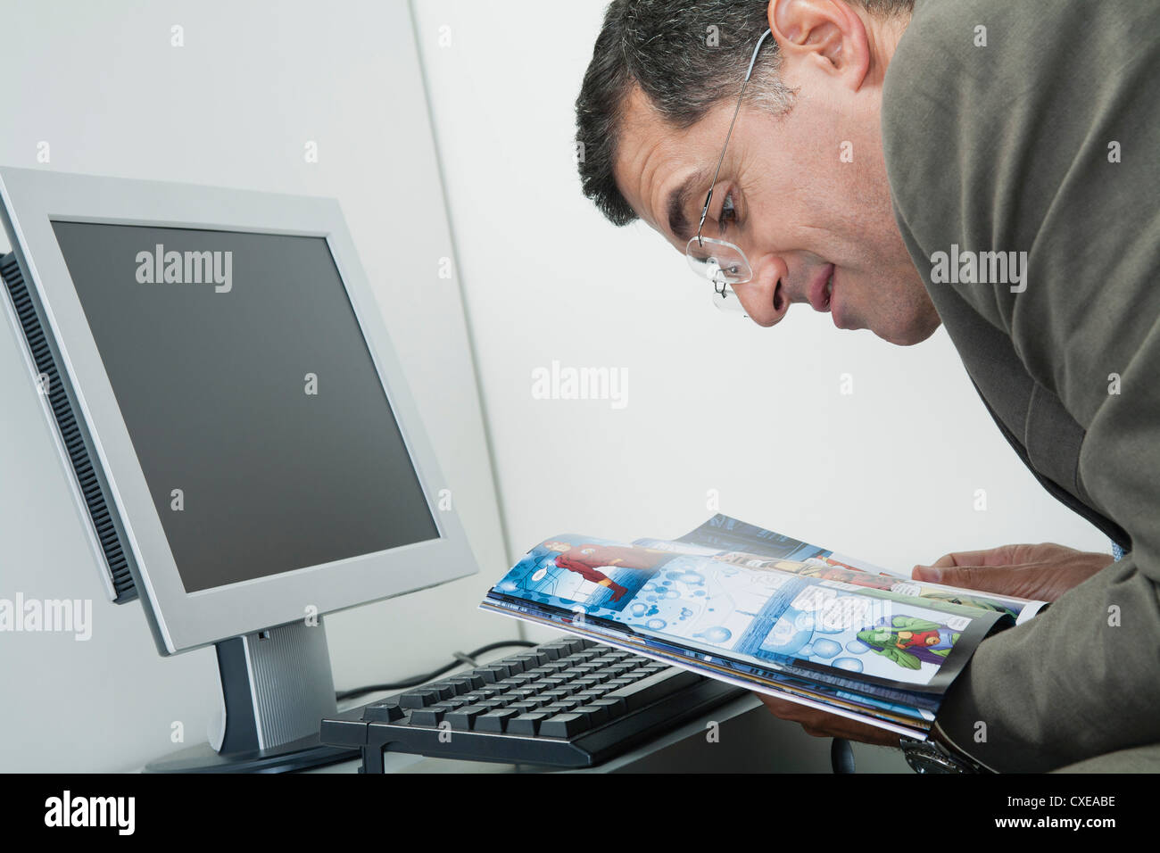 Uomo maturo la lettura del libro di fumetti a scrivania in ufficio Foto Stock