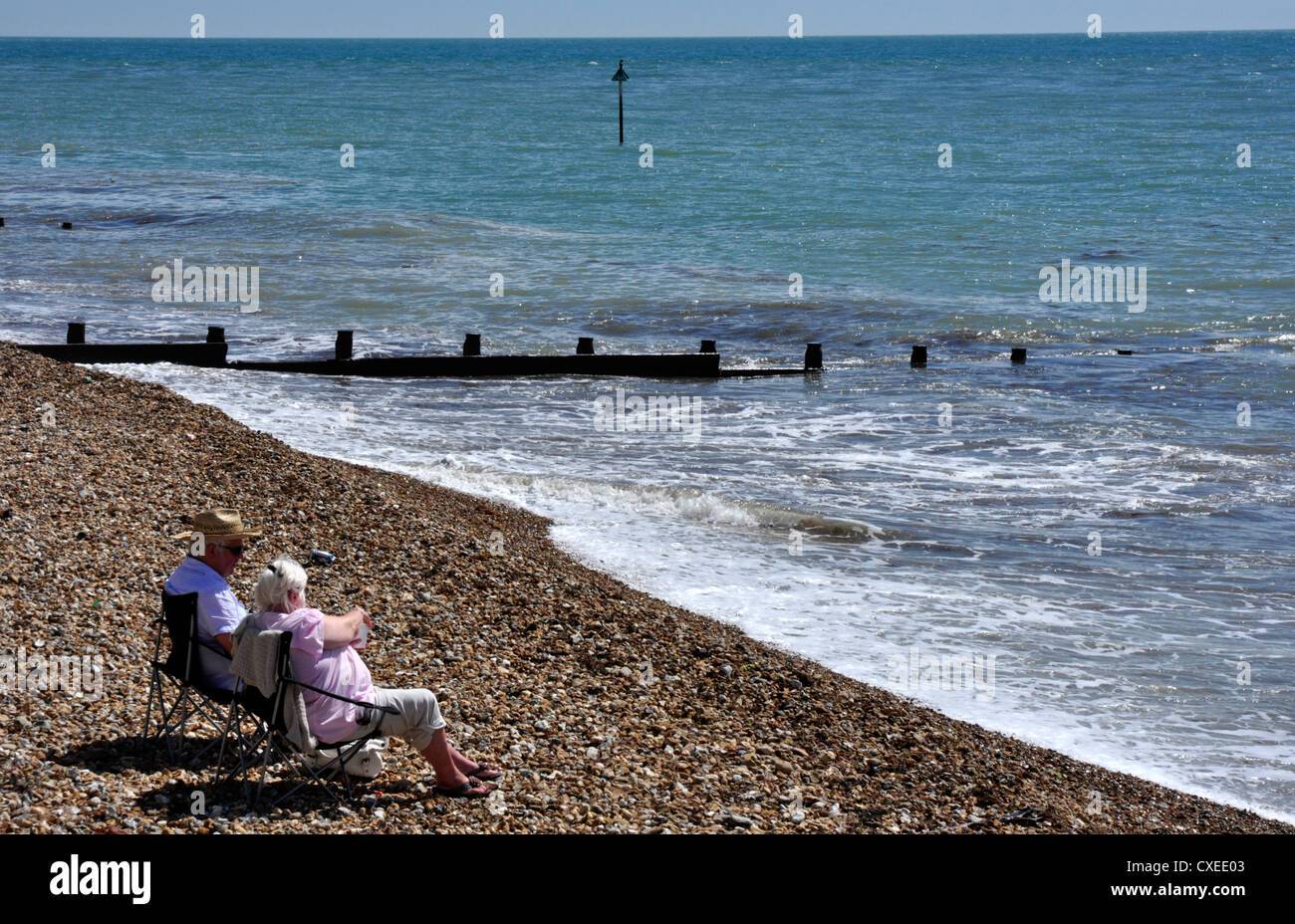 Coppia di anziani godendo di mare e sole - sedie a sdraio sulla spiaggia di ghiaia - dolci onde che lambiscono la riva Foto Stock