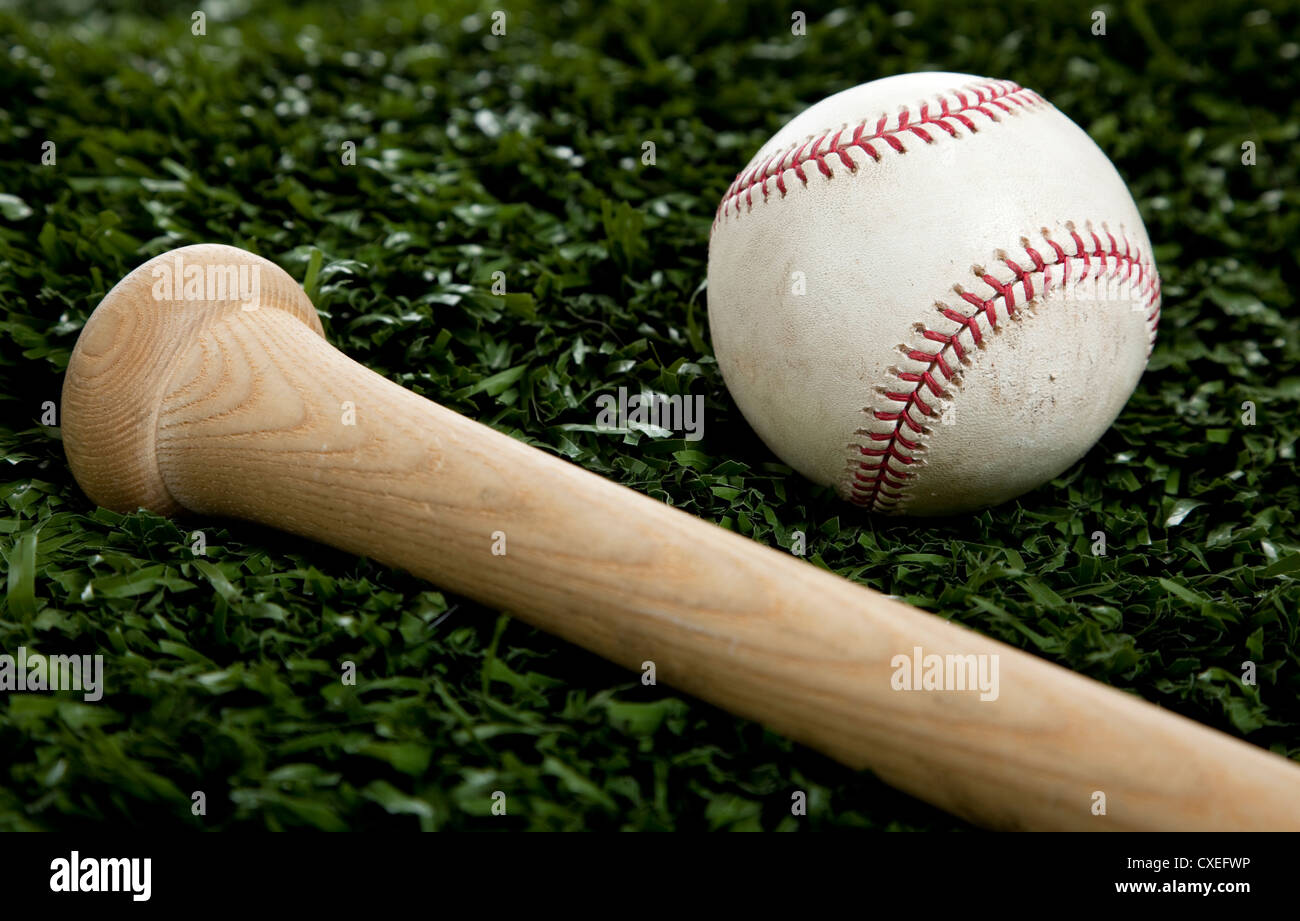 Una estremità di una tavola di legno di mazza da baseball e un baseball bianco su verde erba Foto Stock