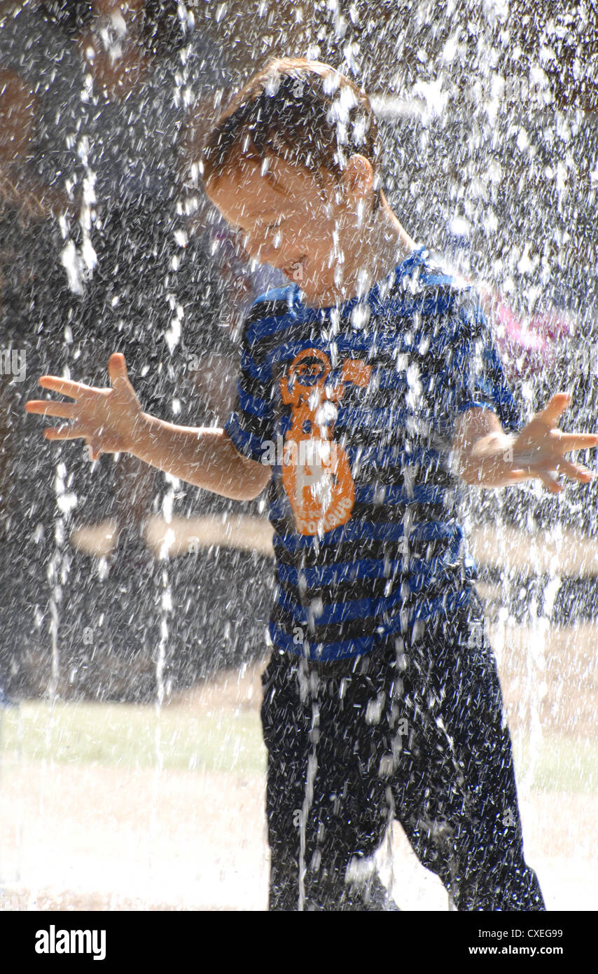 Un giovane ragazzo giocando in una fontana di acqua Foto Stock