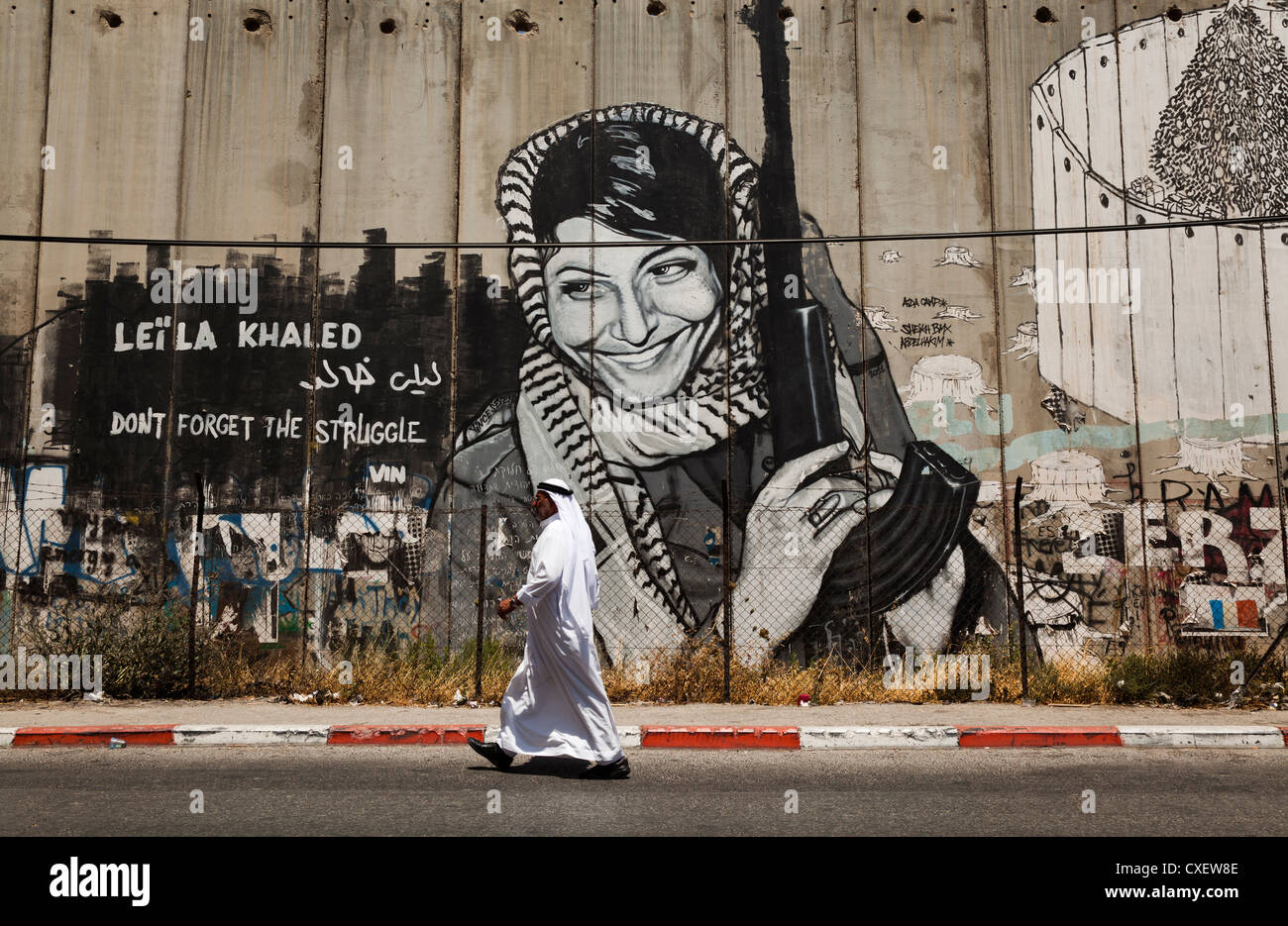 Beduina passeggiate Araba oltre il muro di sicurezza israeliano o 'West Bank barriera divisoria città di Betlemme. Il murale è di Leila Khaled, Foto Stock