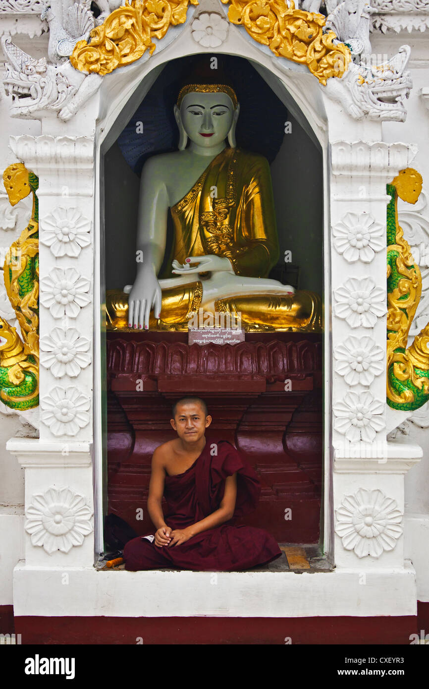 Un giovane monaco si trova al di sotto di una statua del Buddha a Shwedagon Paya o pagoda che risale al 1485 - YANGON, MYANAMAR Foto Stock
