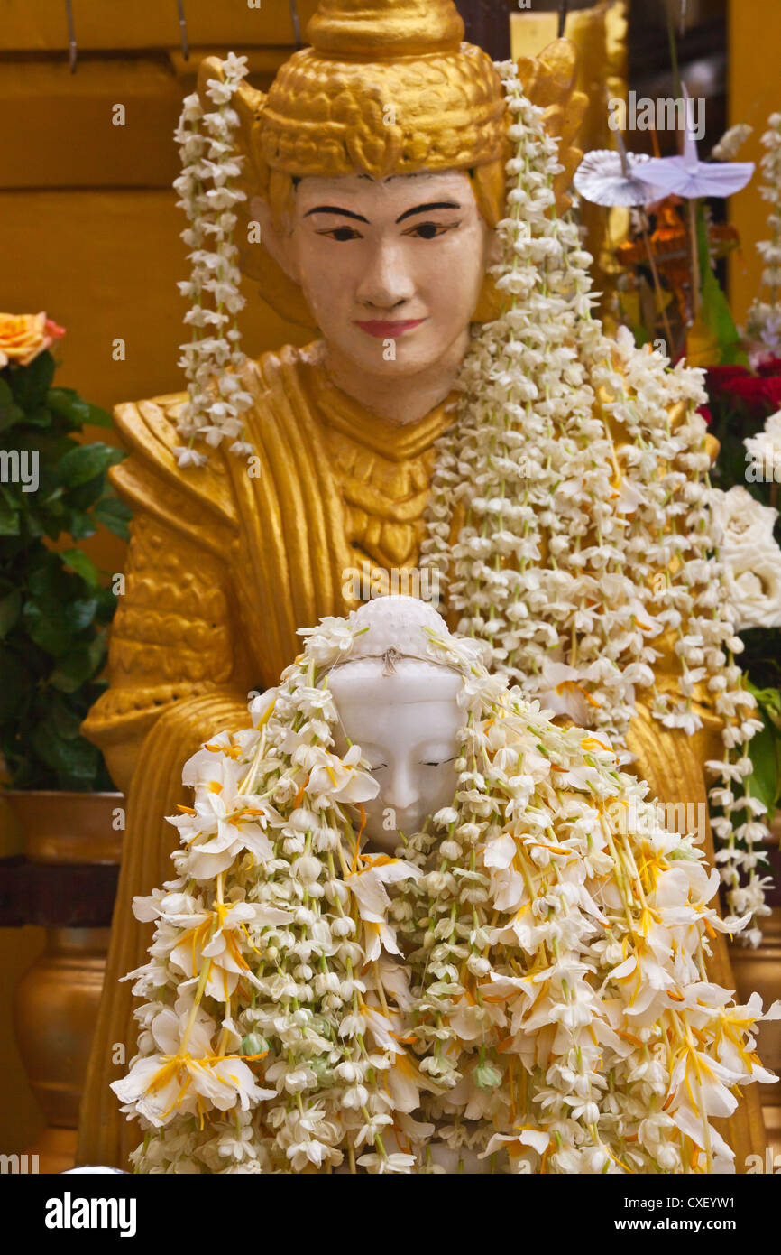 Una statua di Buddha ricoperta di fiori alla Shwedagon Paya o pagoda che risale al 1485 - YANGON, MYANMAR Foto Stock