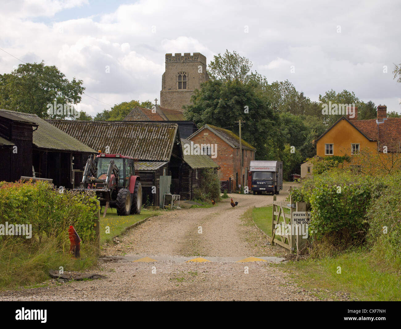 Una scena di un paese di lingua inglese cortile, con annessi, trattore, galline e polli e torre di una chiesa. Foto Stock