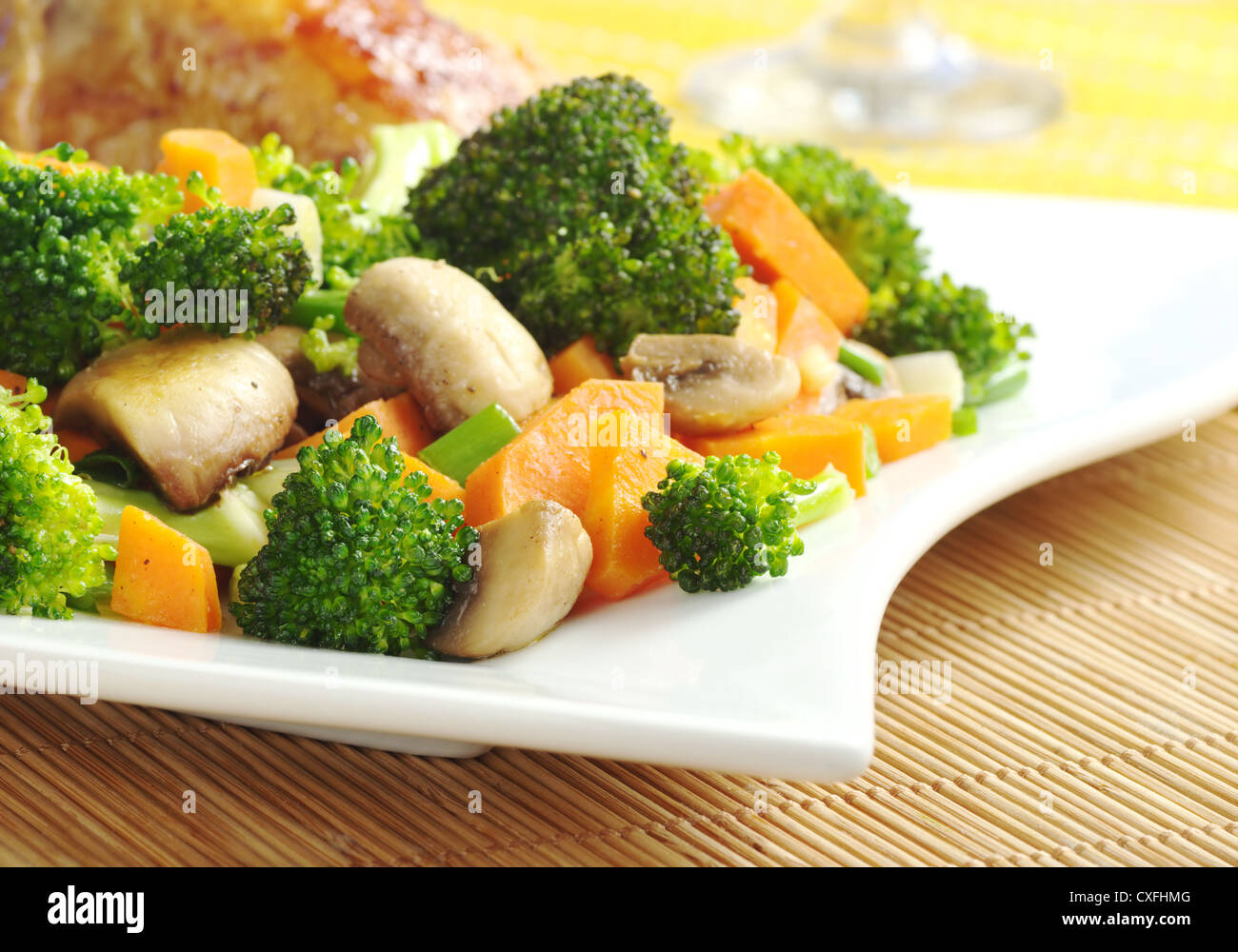 Verdure fritte (broccoli, i funghi, la carota, scalogno) sulla piastra bianca con carne di pollo e bicchiere di vino in background Foto Stock