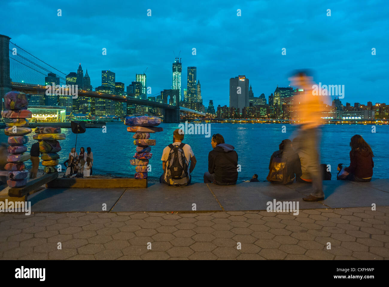 New York City, NY, STATI UNITI D'AMERICA, i turisti seduti a guardare lo skyline di Manhattan al crepuscolo da DUMBO Ponte di Brooklyn Park Foto Stock