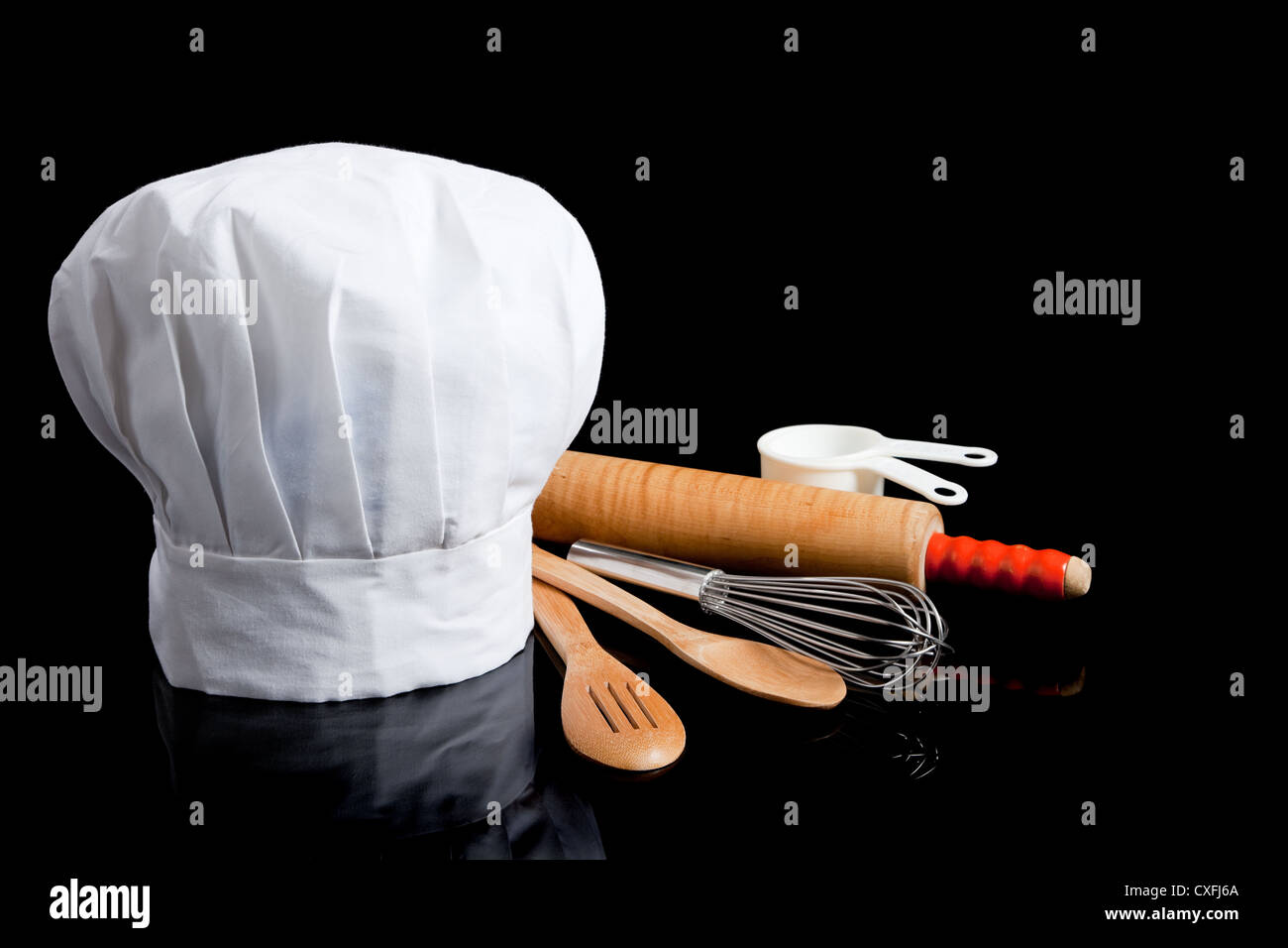 Un chef hat con utensili di cottura su un fondo nero con spazio di copia Foto Stock