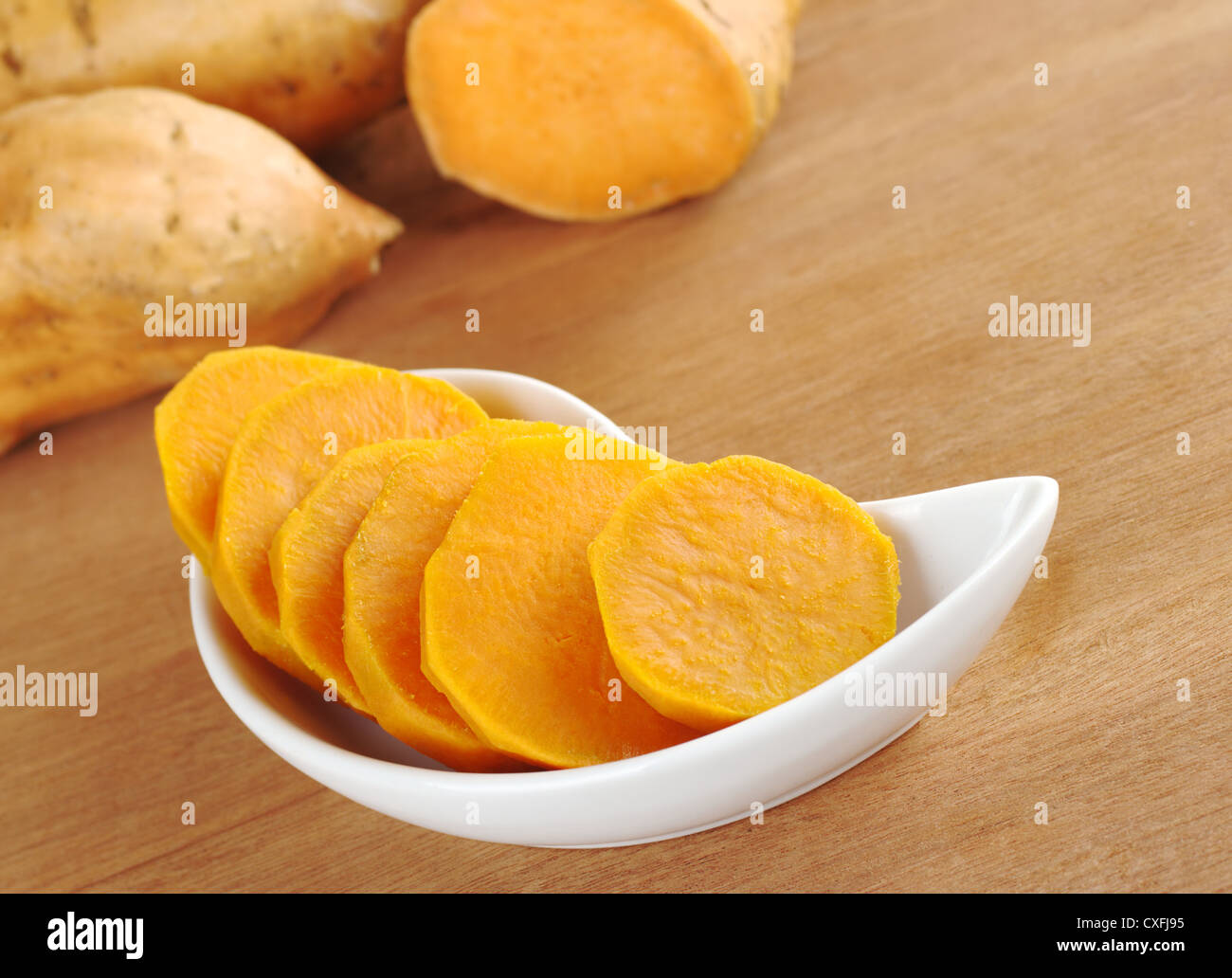 Cuocere la patata dolce (lat. Ipomoea batatas) tagliato a fette nella ciotola bianco su una superficie di legno con materie prime patate dolci nel retro Foto Stock