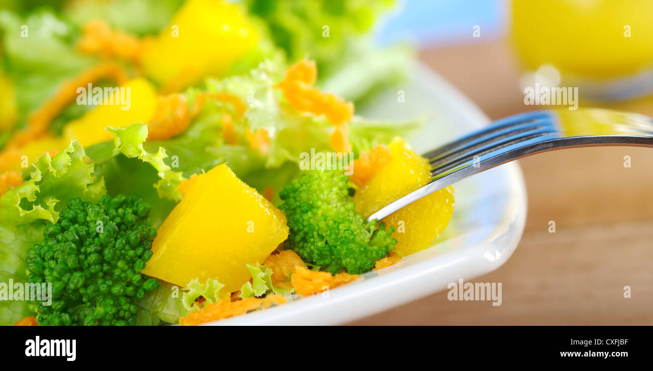 Fresco e leggero broccoli-mango-Insalata di carote sulla piastra bianca con un pezzo di mango sulla forcella Foto Stock