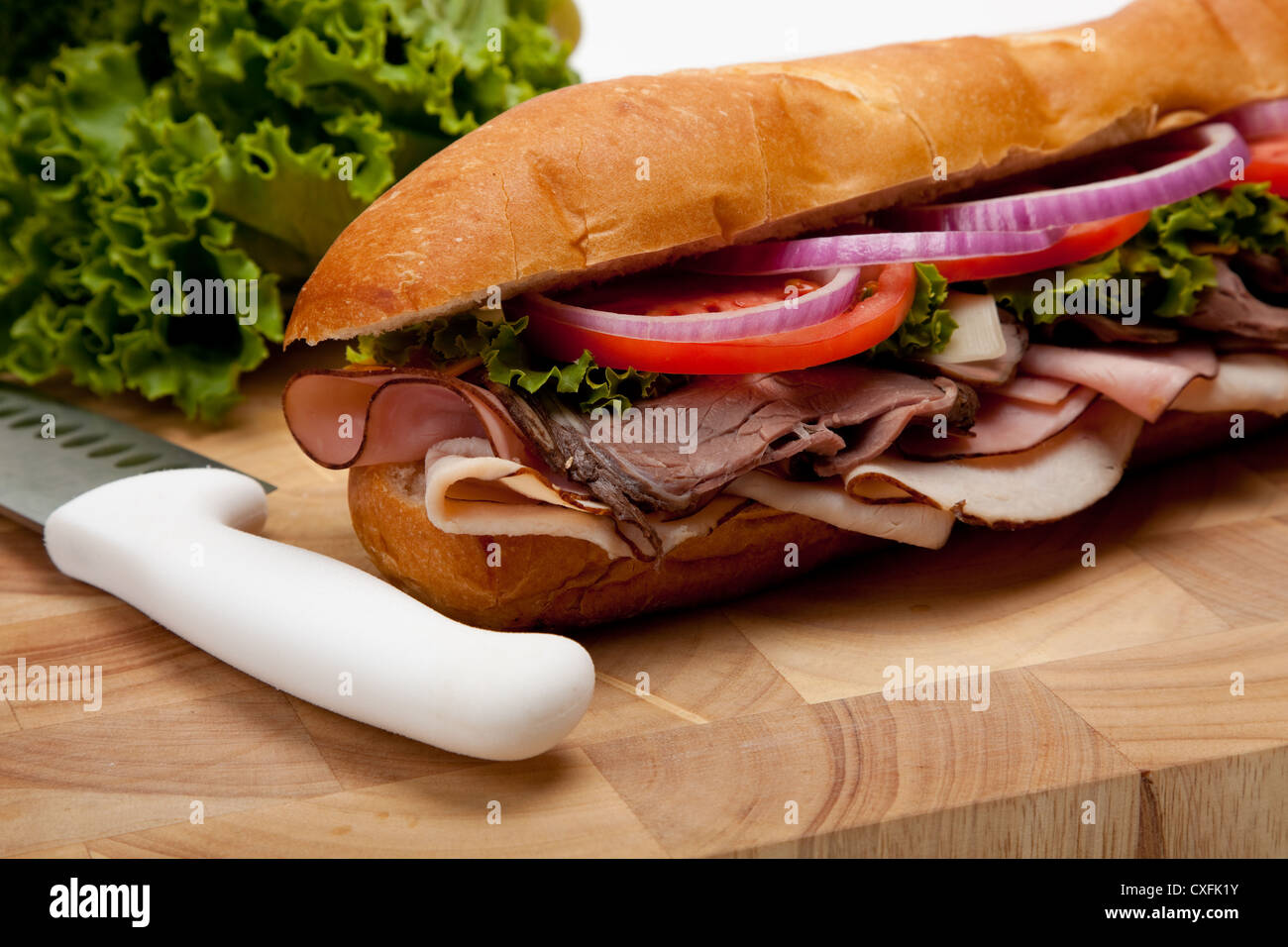 Sandwich sottomarino su un tagliere con un coltello e lattuga Foto Stock