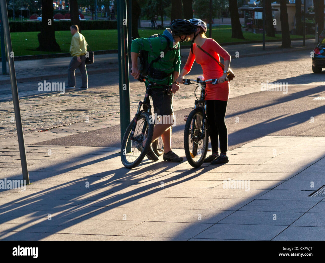 KISS MEET STREET due ciclisti si fermano per baciare teneramente incontrarsi e salutare sul marciapiede della città illuminato dal sole Foto Stock