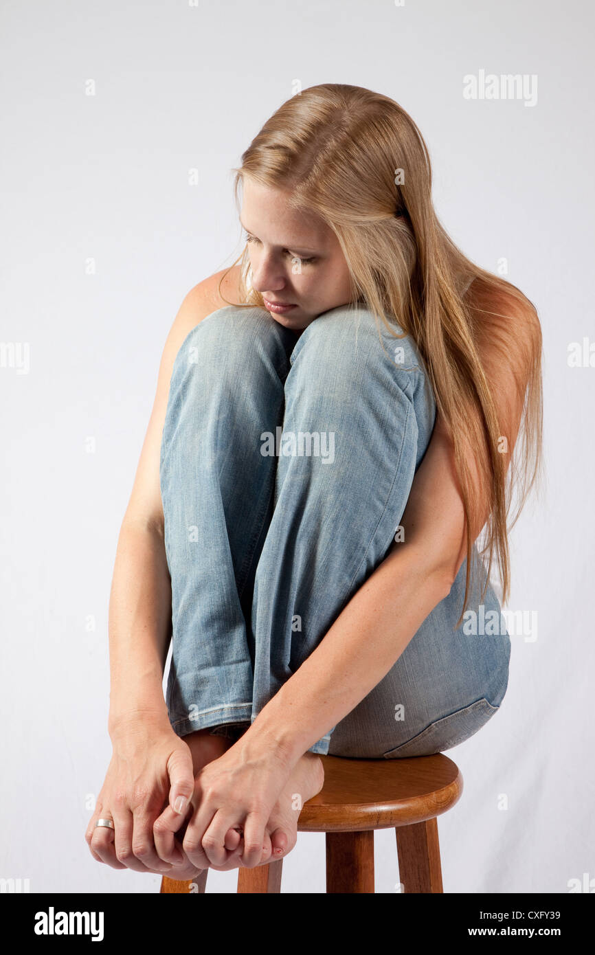 Bella donna bionda seduto con il ginocchio sollevato fino vicino al suo mento, guardando la telecamera con un attenta occhiata Foto Stock