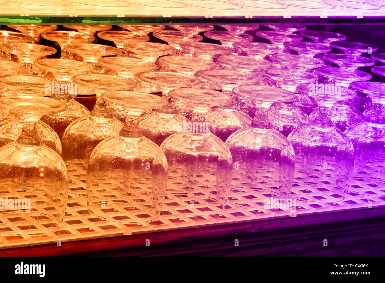 Una immagine di sfondo di bicchieri su un ripiano di pub che è illuminato da luci colorate Foto Stock