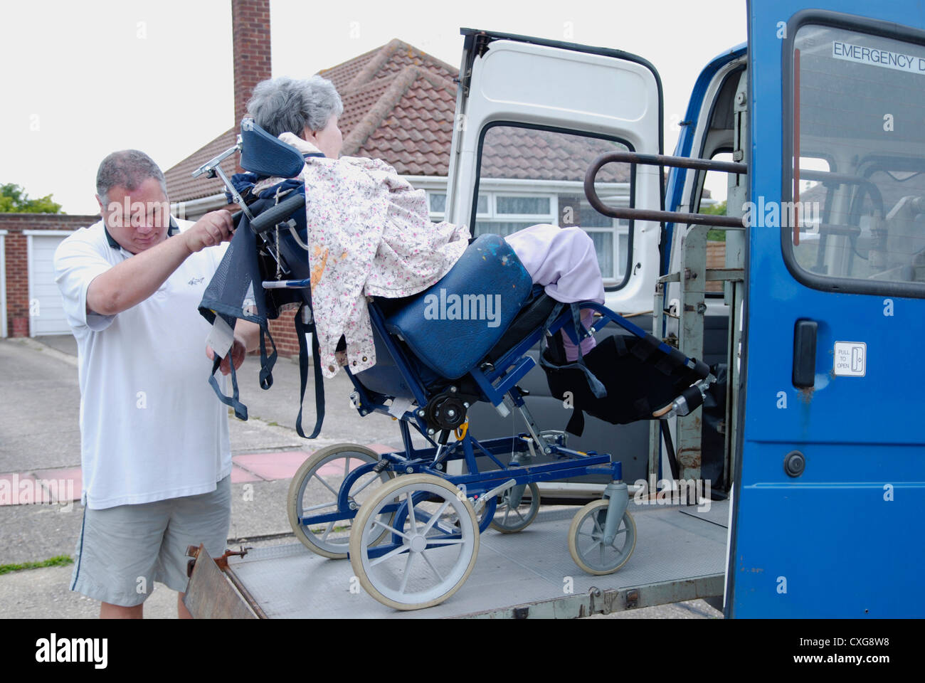 Donna anziana in una sedia a rotelle sulla piattaforma di sollevamento Rampa specialistico di un veicolo adattato per il servizio volontario per il trasporto di disabili Foto Stock