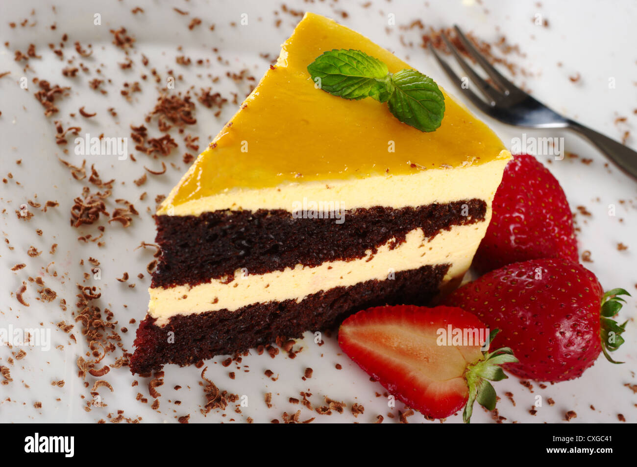 Un pezzo di lucuma (Sud Americana frutto) torta guarnite con foglie di menta, scaglie di cioccolato e fragole Foto Stock