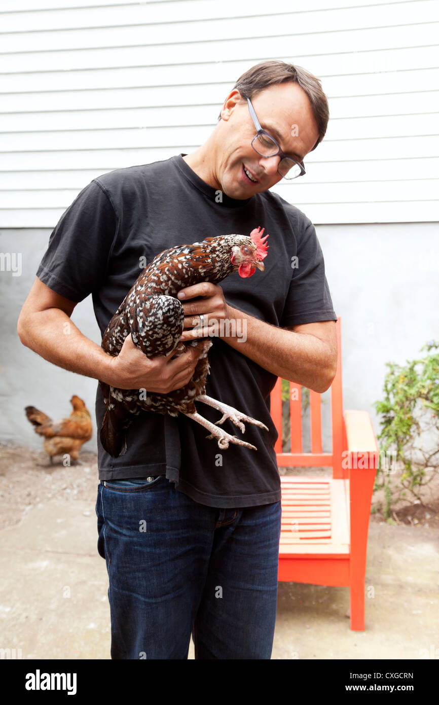 Un uomo è in possesso di un pollo nel suo cortile. Foto Stock