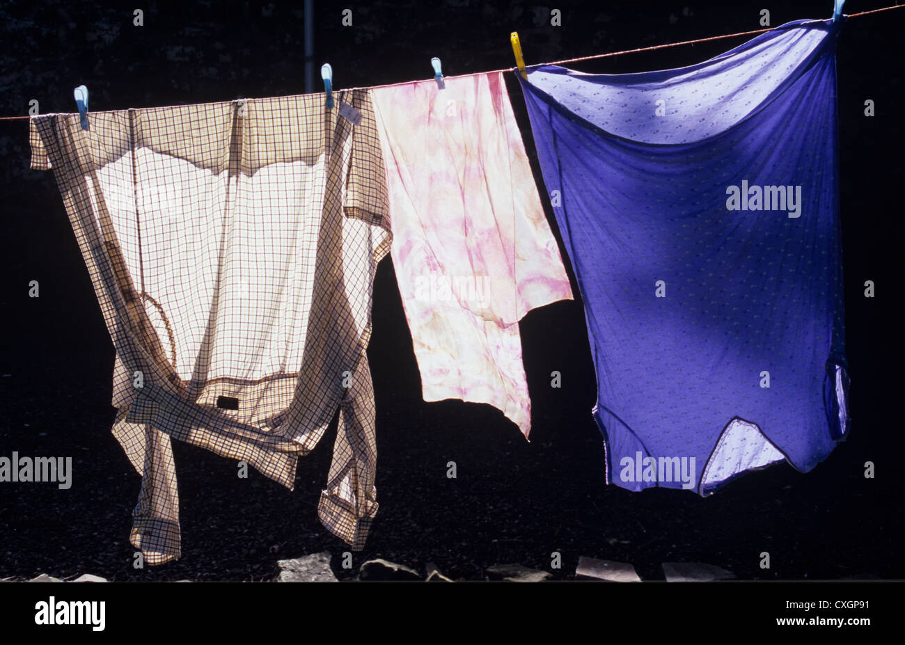 Maglietta e sciarpa e nightshirt appesi ad asciugare sul lavaggio-riga retroilluminato luminosamente contro il muro oscuro Foto Stock