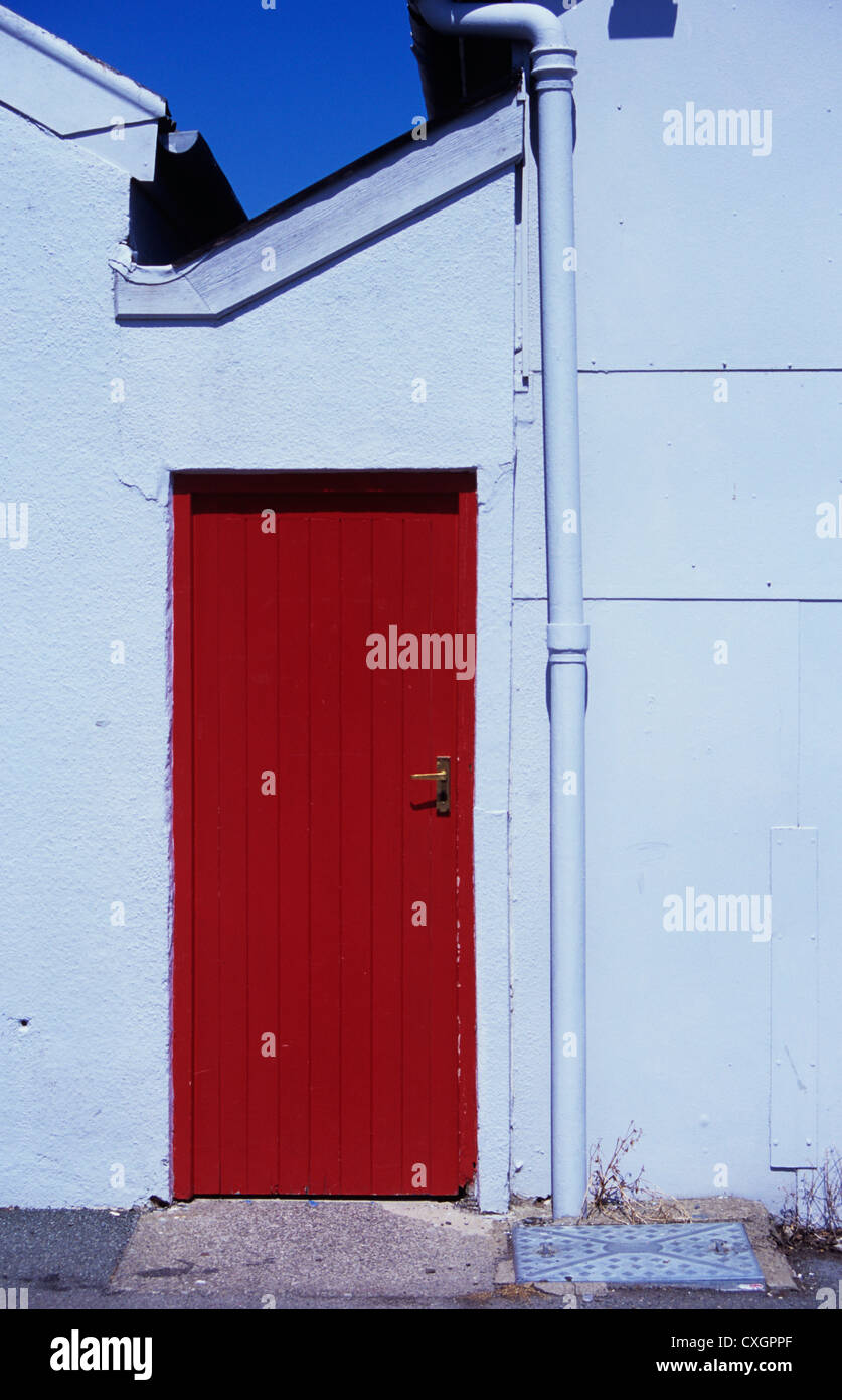 Dipinto di rosso porta in legno nel corridoio con tetto spiovente tra due parti del dipinto di bianco di fabbrica o magazzino Foto Stock