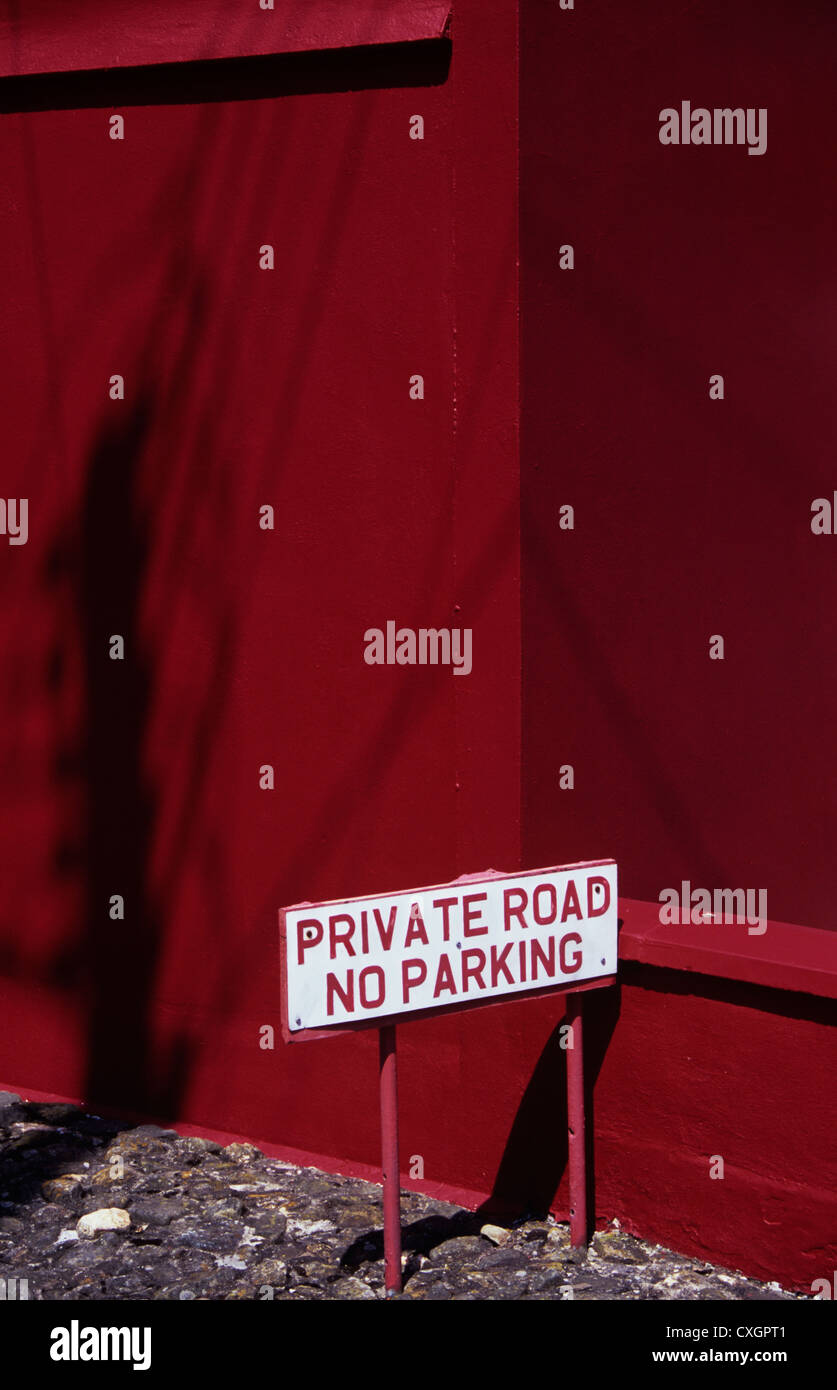 Dettaglio della parete e edificio dipinto di rosso con un palo telefonico ombra e segno di unità su strada privata senza parcheggio Foto Stock