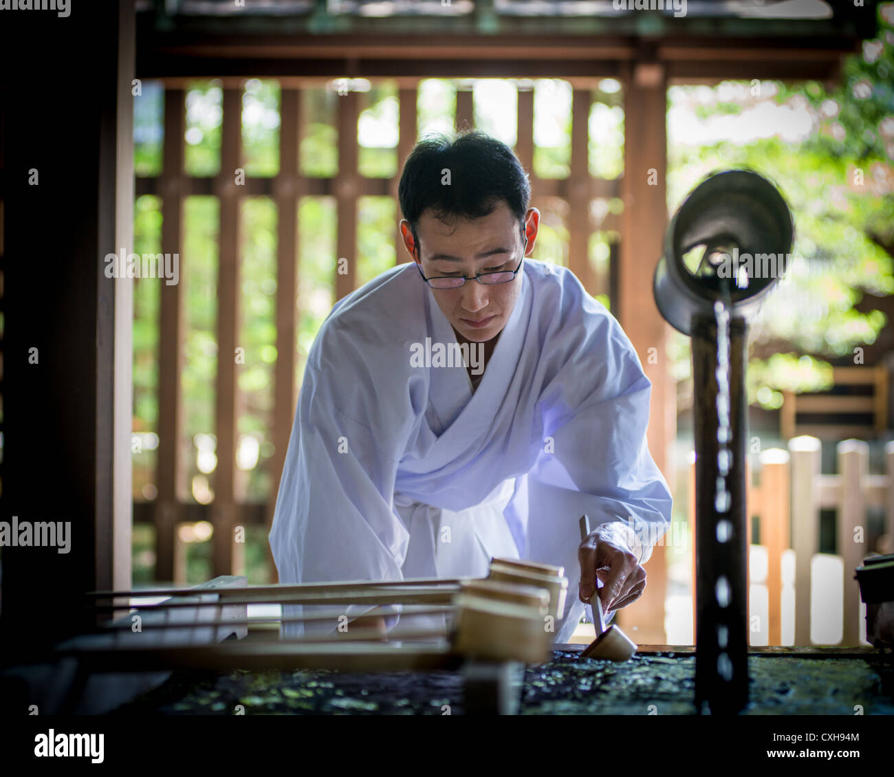 Un sacerdote scintoista salse acqua da un serbatoio tramite una siviera di bambù al Tempio di Meiji, Tokyo, Giappone Foto Stock