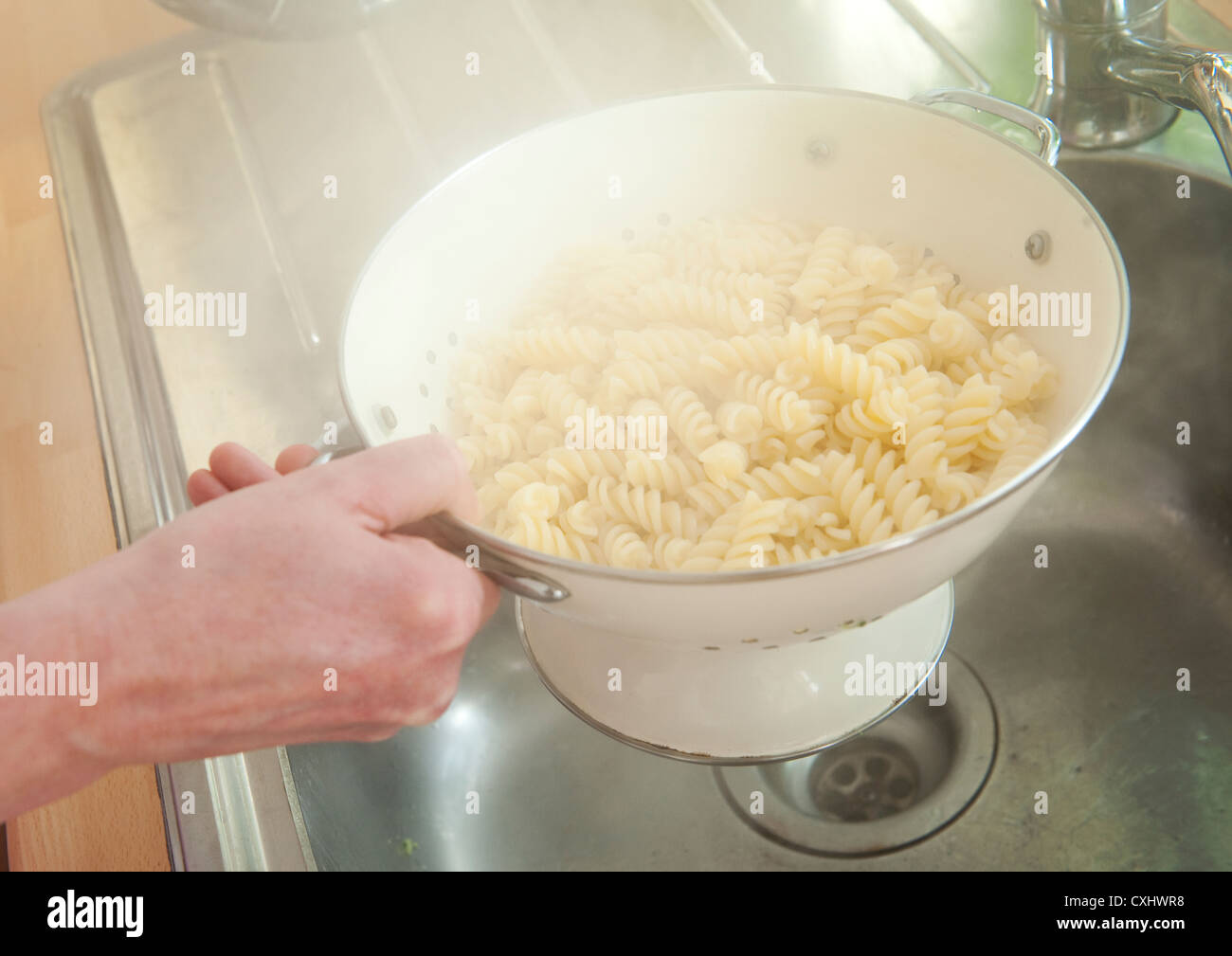 Aumento di vapore dalla pasta viene scaricato in uno scolapasta sopra un lavello da cucina. Foto Stock
