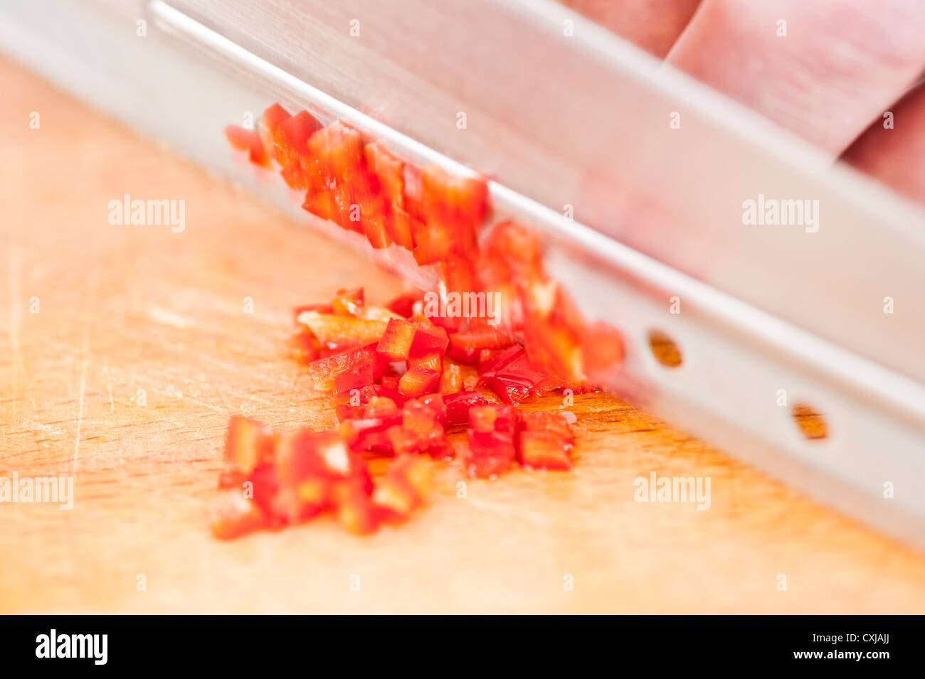 Vista dettagliata del peperoncino rosso tritato essendo da uno chef su un tagliere di legno Foto Stock