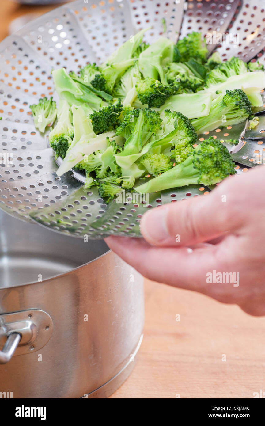 Primo piano di cottura uomo broccoli, preparazione del vegetale in una pentola con un sistema di cottura a vapore utensile Foto Stock