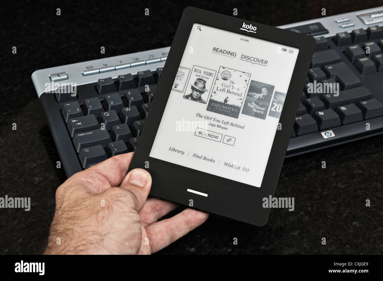 Un uomo tiene e legge un Kobo touch ereader (ebook) vicino alla tastiera di un computer. Foto Stock