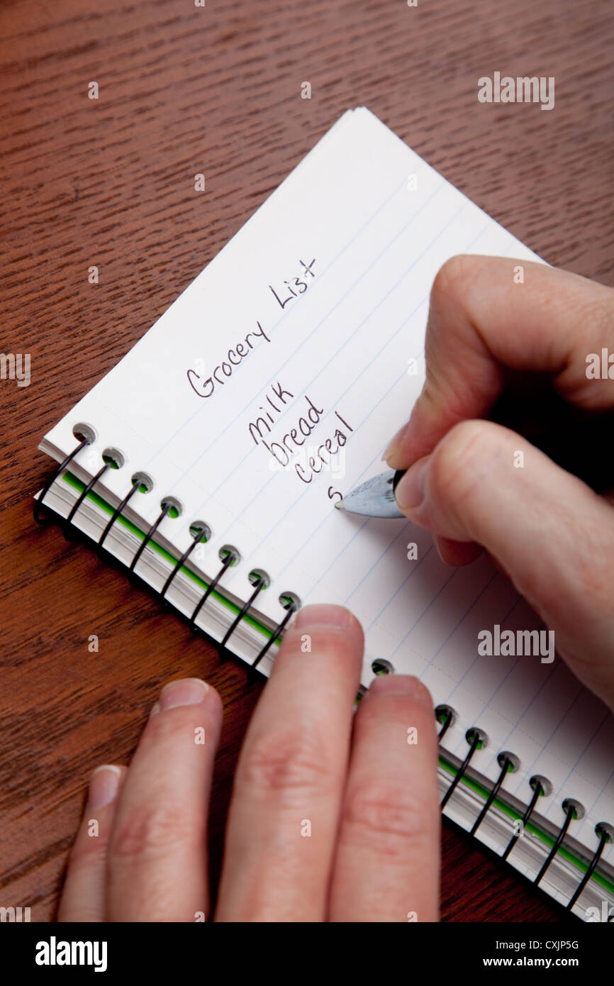 La donna a scrivere una lista della spesa su un notebook a spirale con un tavolo di legno sfondo Foto Stock