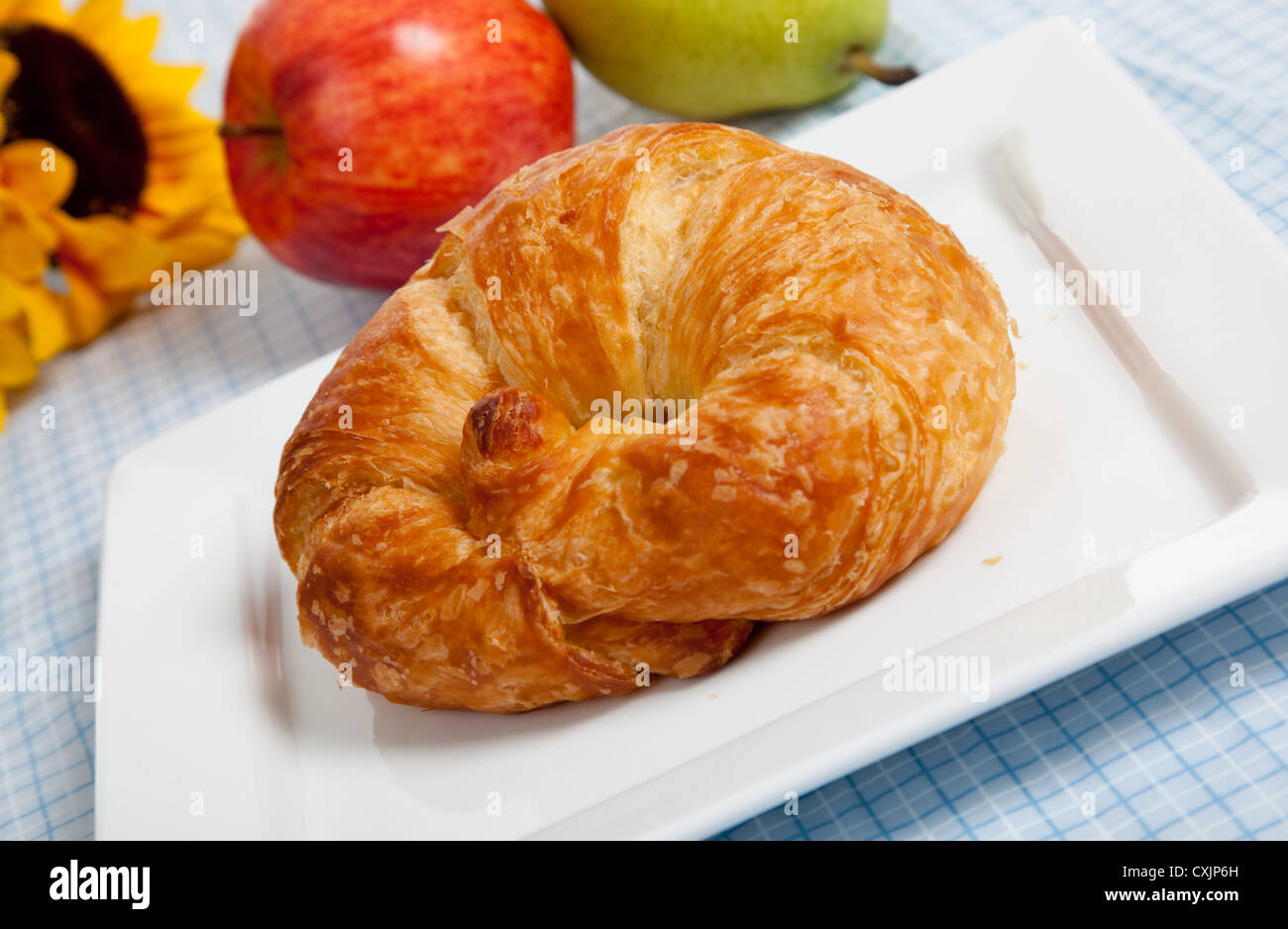 Croissant francesi su una piastra bianca con mele e un girasole su un gingham blu tovaglia Foto Stock
