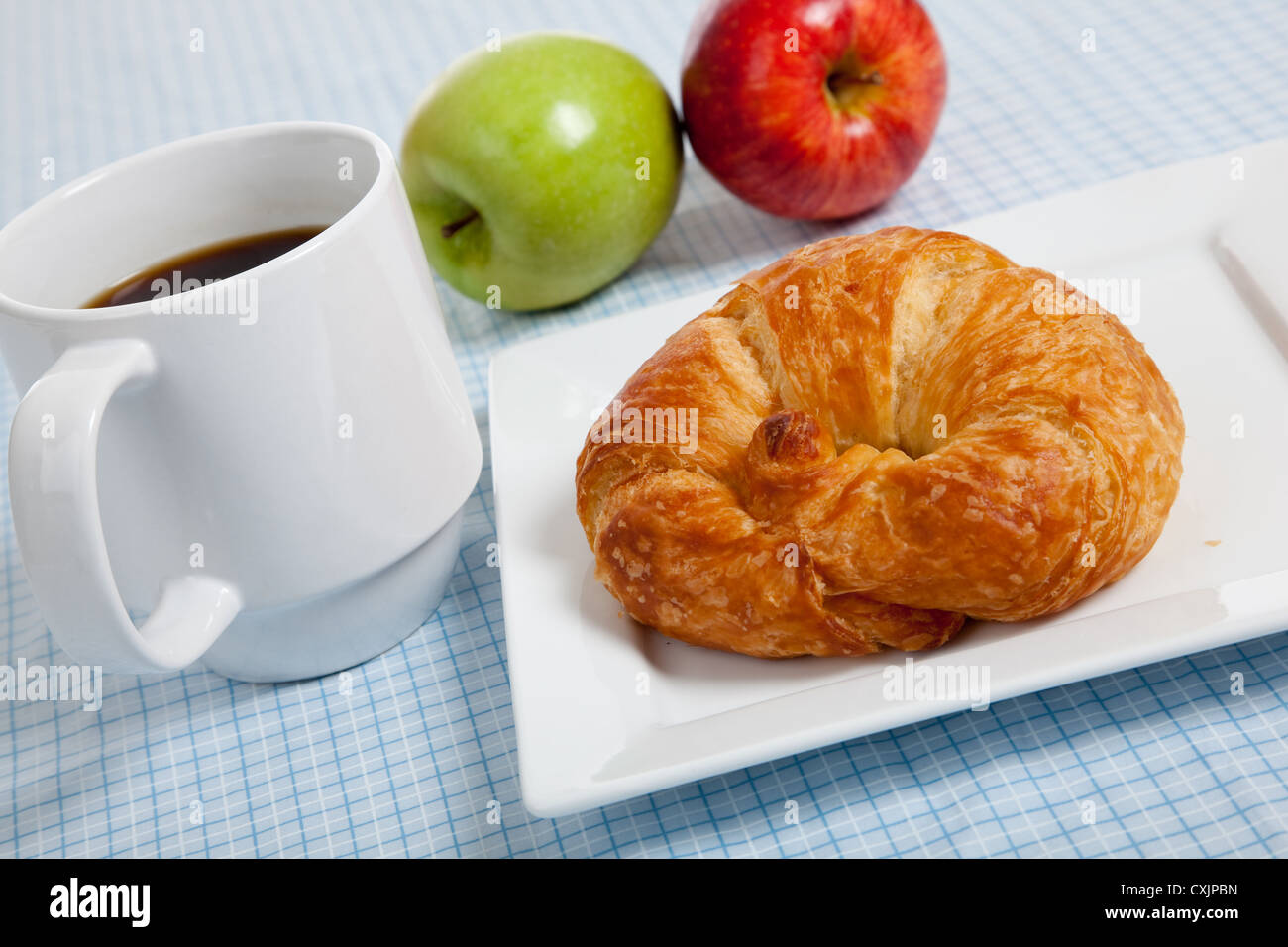 Croissant francesi su una piastra bianca con tazza di caffè e le mele su un gingham blu tovaglia Foto Stock