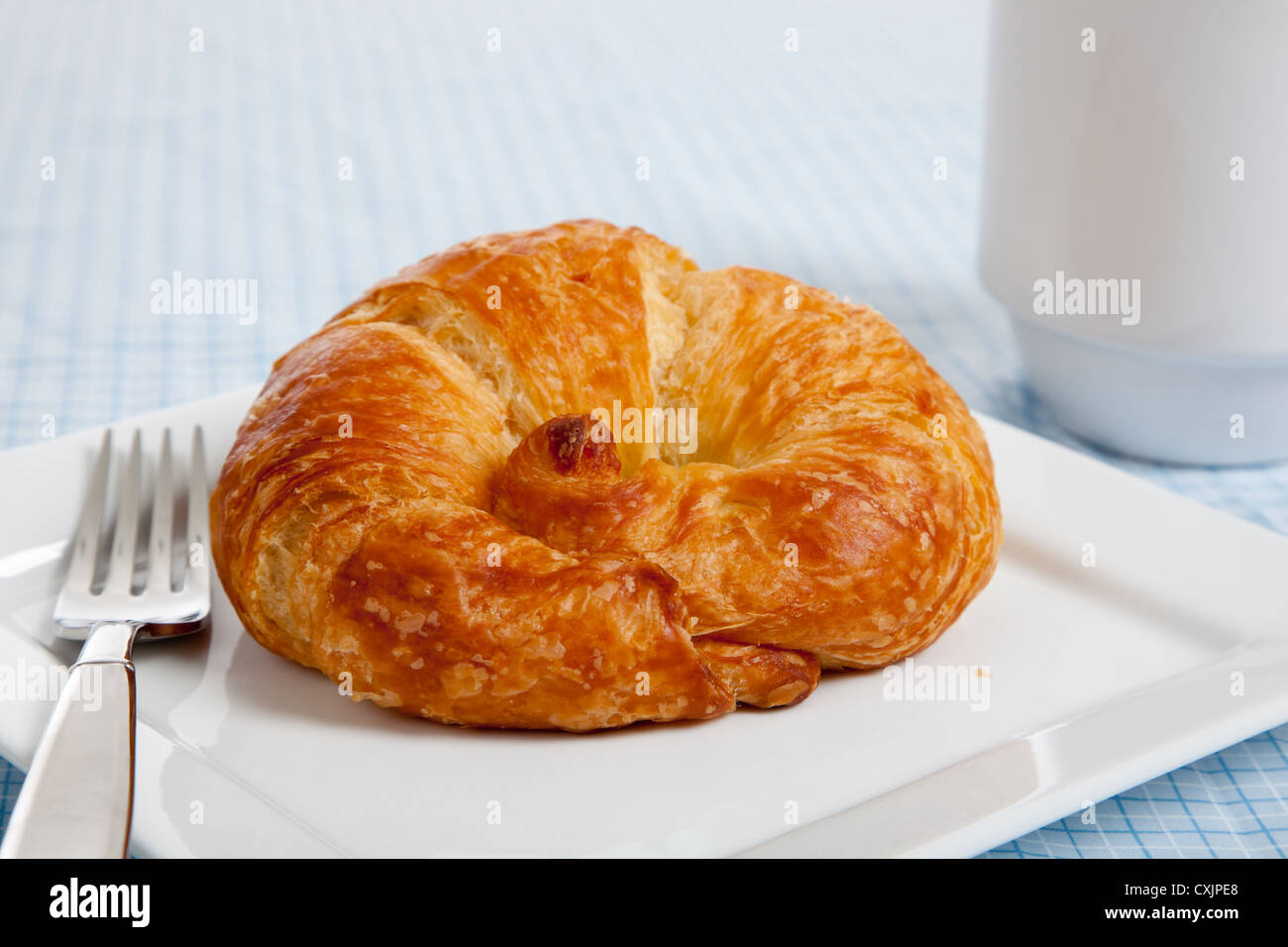 Croissant francesi su una piastra bianca con tazza di caffè e la forcella su un gingham blu tovaglia Foto Stock