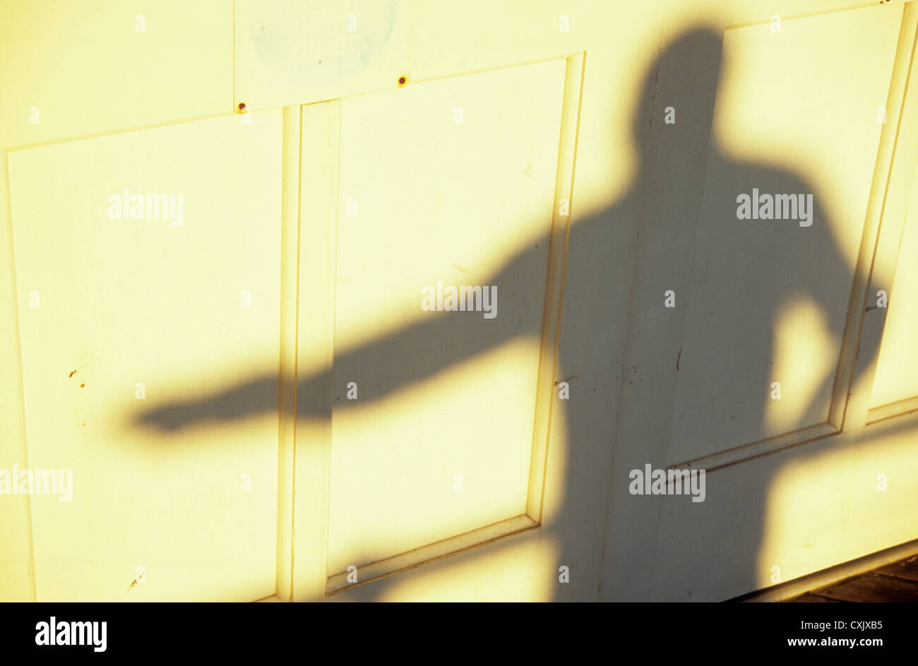 Ombra nella calda luce su bianco pannelli dipinti di uomo con un braccio su ringhiere e altro braccio proteso Foto Stock