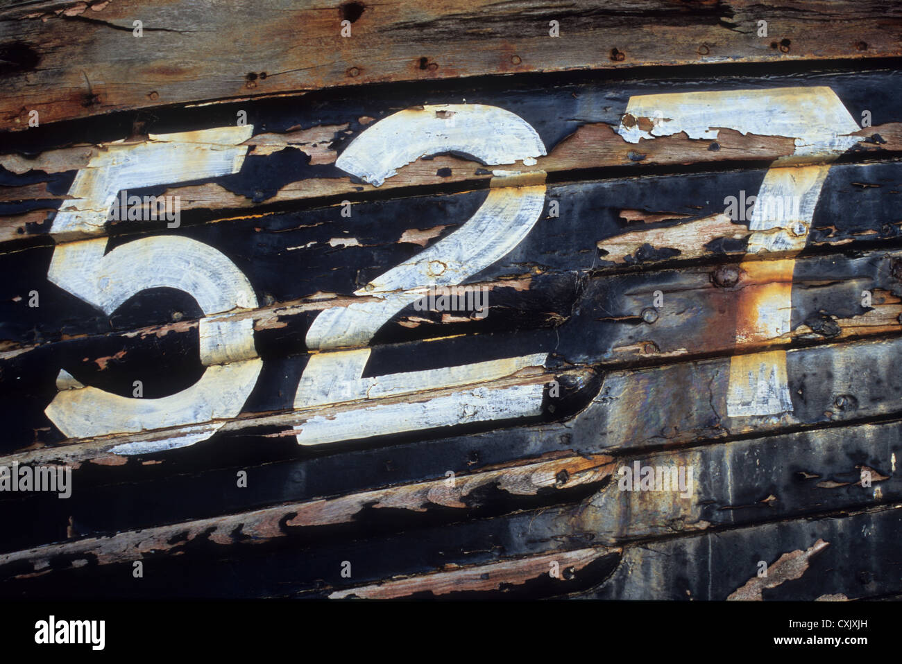 Dettaglio del lato della barca di legno con sfald vernice nera e numeri 527 verniciato in bianco Foto Stock