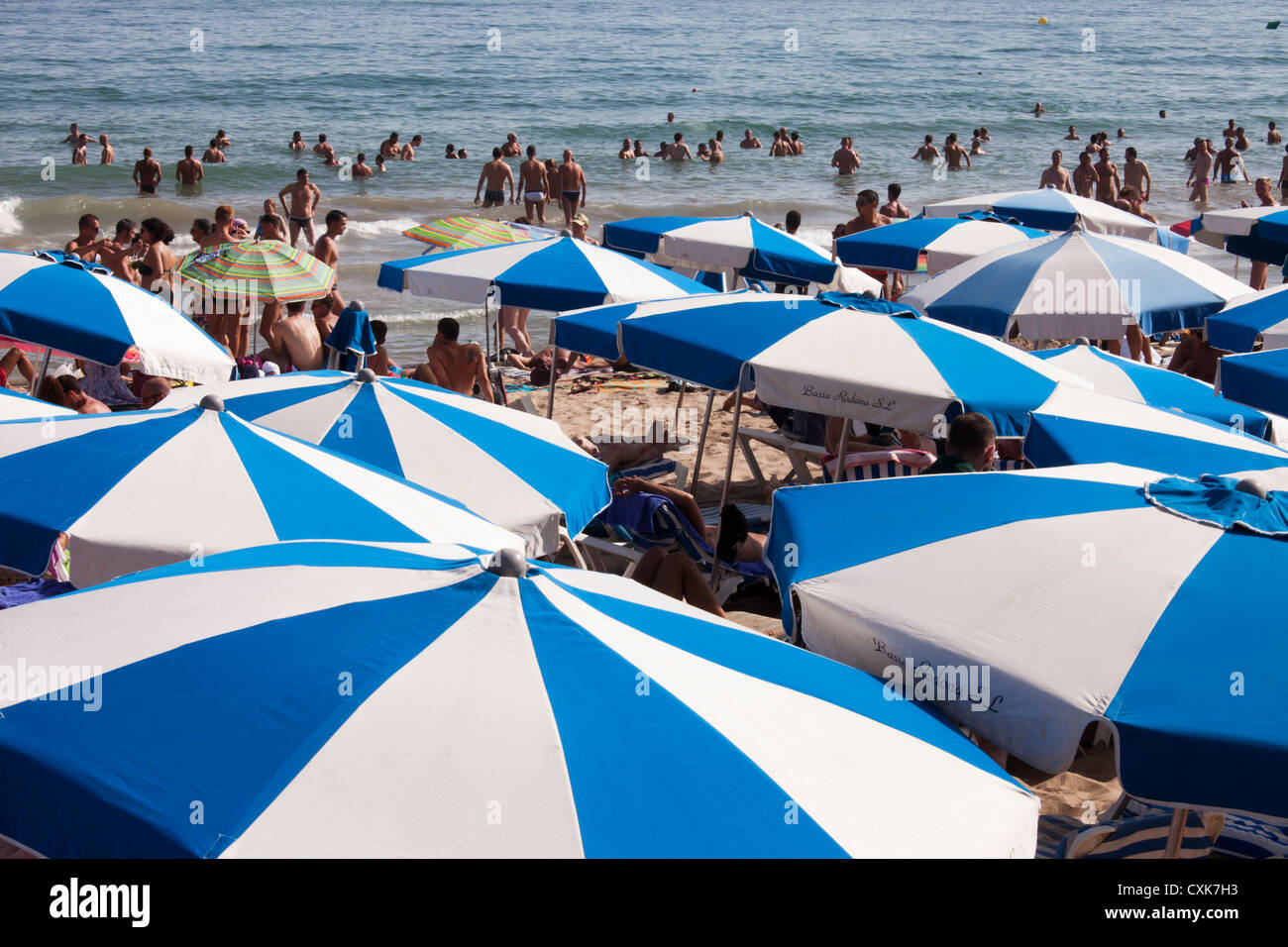 Una folla di prevalentemente uomini al gay area della spiaggia di Sitges soggiorno sotto gli ombrelloni o andare a nuotare. Foto Stock