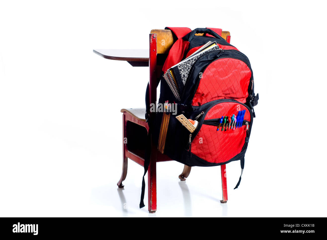 Un rosso, vintage banco di scuola su uno sfondo bianco, con un rosso zaino colmo di forniture scolastiche Foto Stock